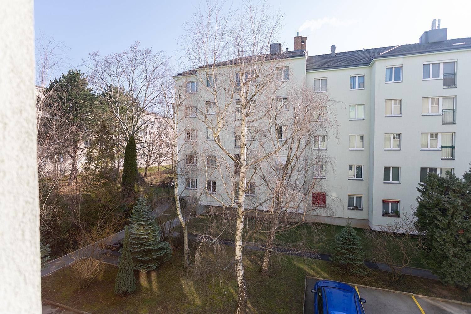 Blick auf die Gebäudefassade und den begrünten Innenhof mit Bäumen und Parkplätzen.