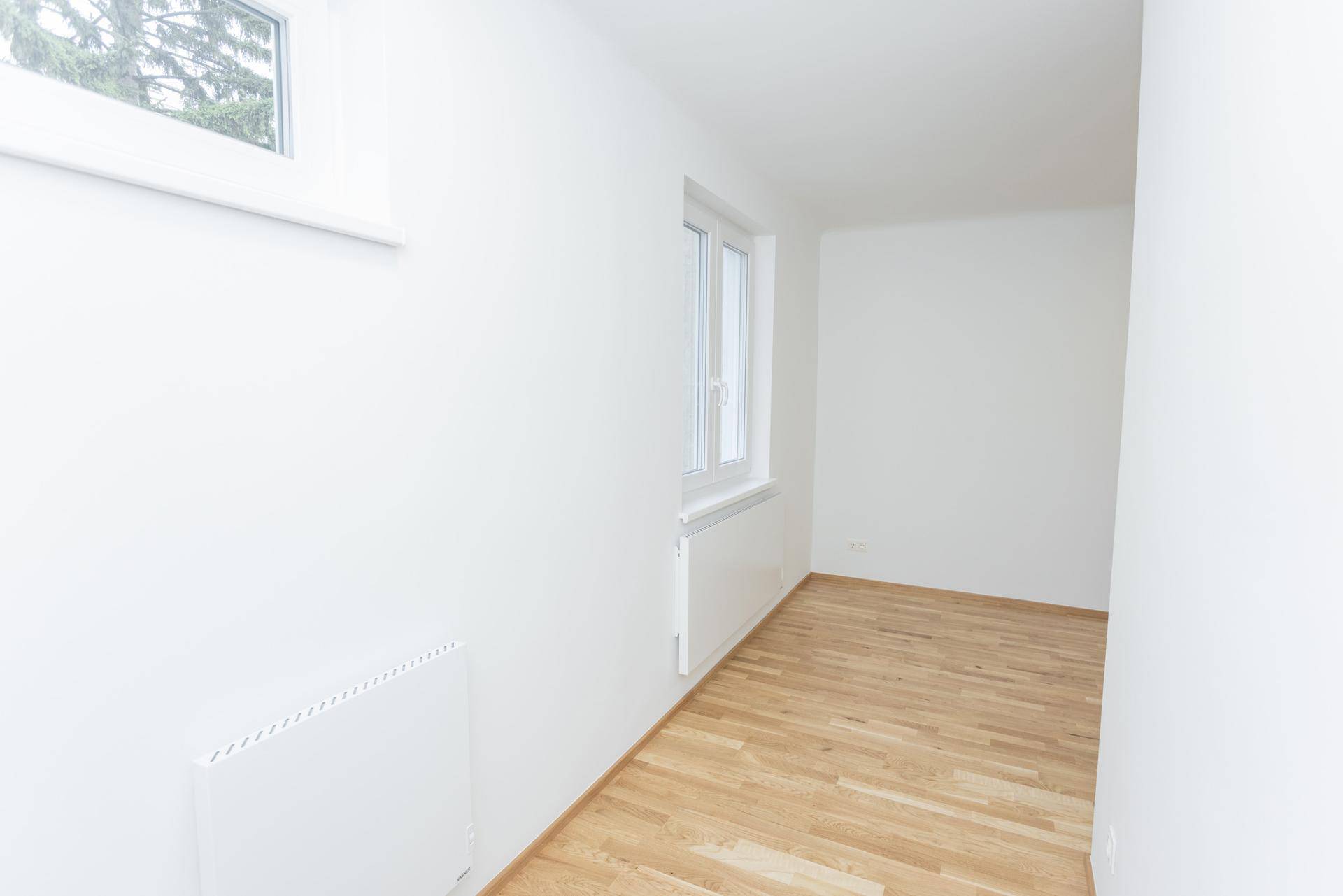 Heller, leerer Raum mit Holzboden und zwei Fenstern, bietet viel Tageslicht.