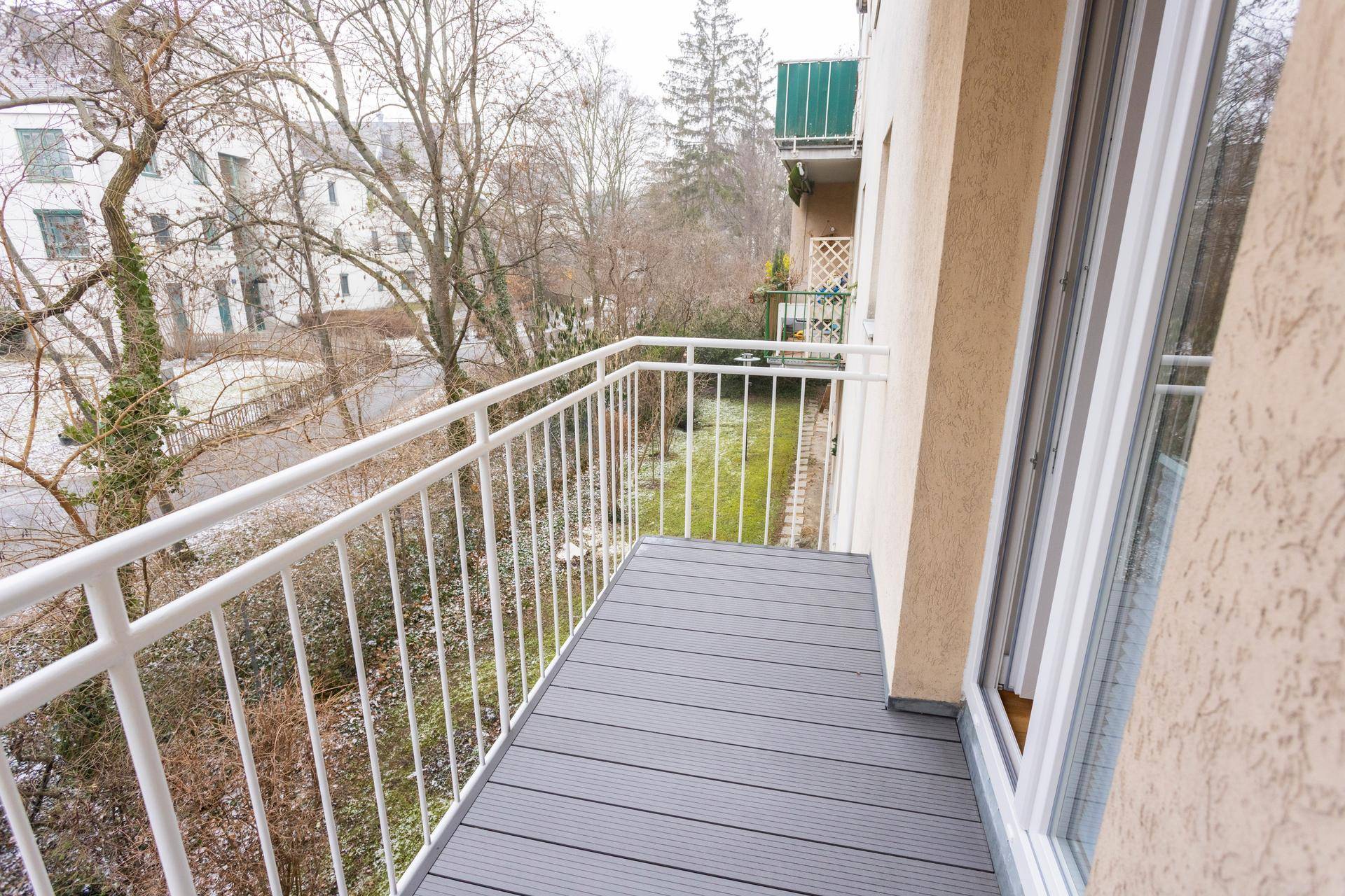 Balkon mit grauen Dielen und weißem Geländer, bietet einen Blick ins Grüne.
