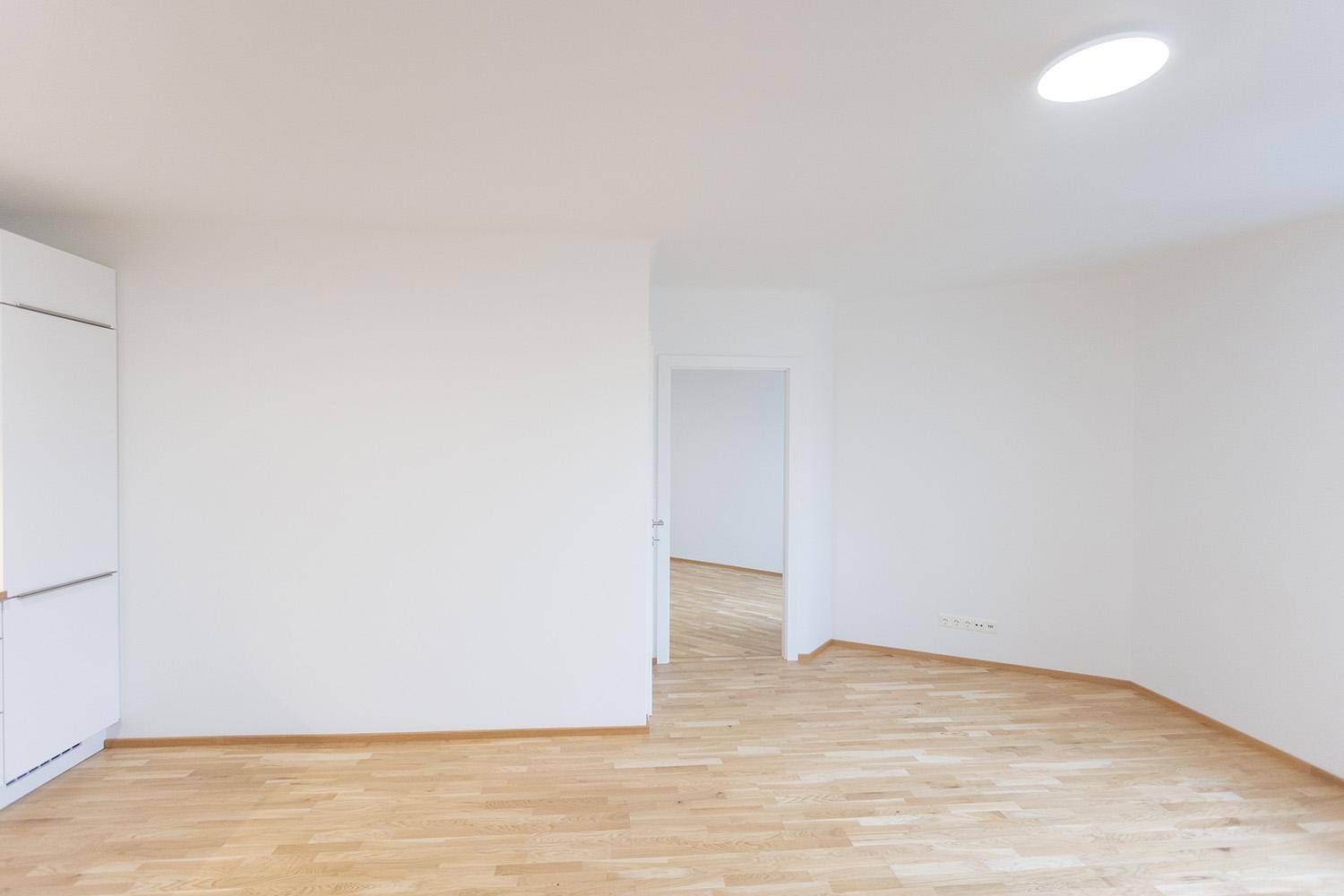 Geräumiger, heller Wohnbereich mit Holzboden und weiß gestrichenen Wänden, ideal für individuelle Einrichtung.