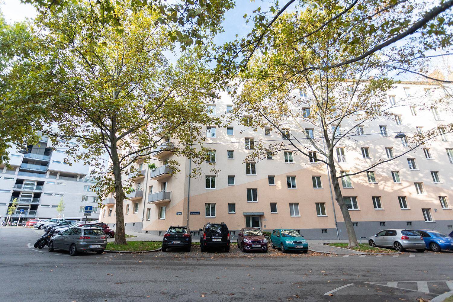 Außenansicht eines Mehrfamilienhauses mit Bäumen und Parkplätzen in städtischer Umgebung.