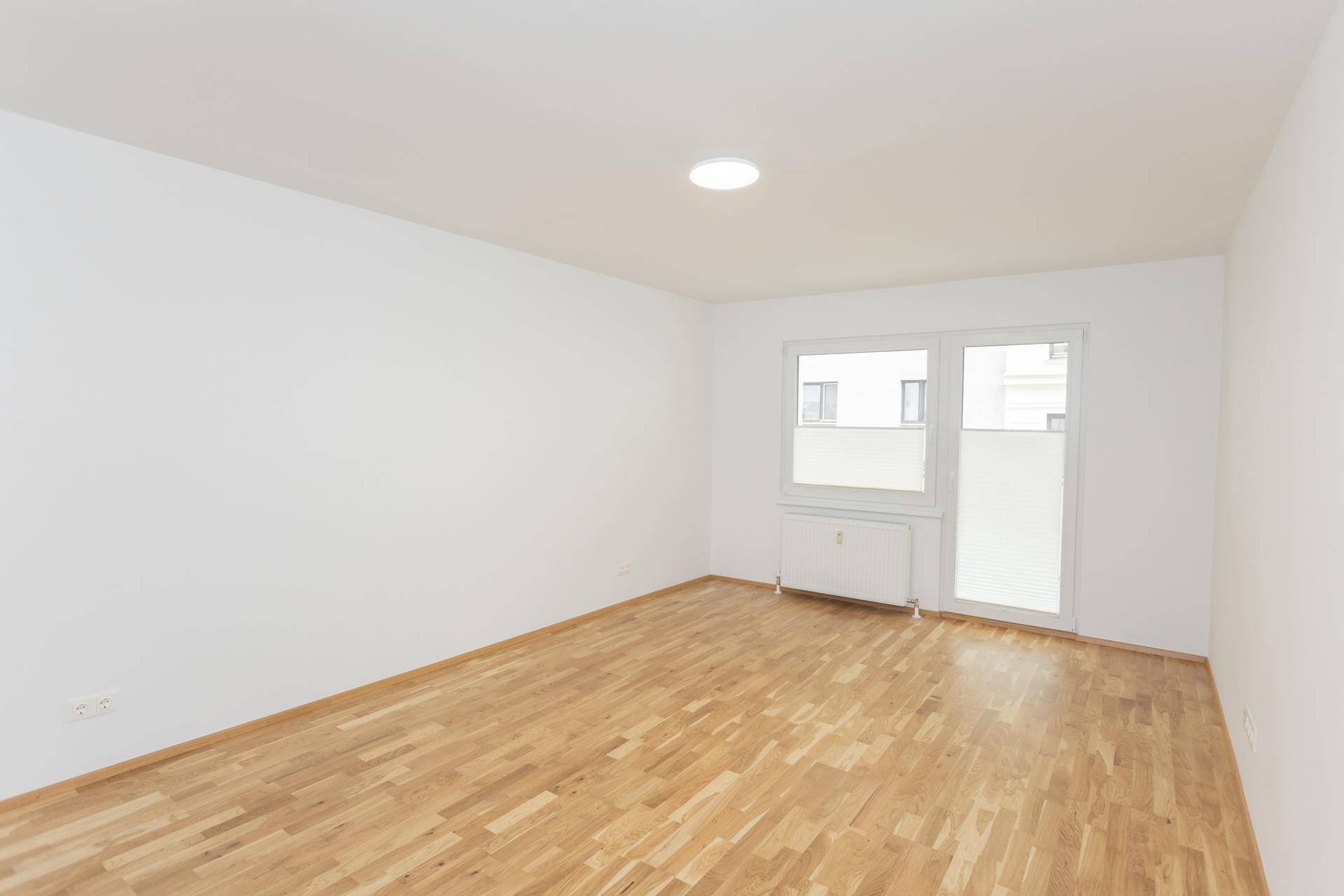 Helles Zimmer mit Parkettboden und großem Fenster, das viel Tageslicht hereinlässt.