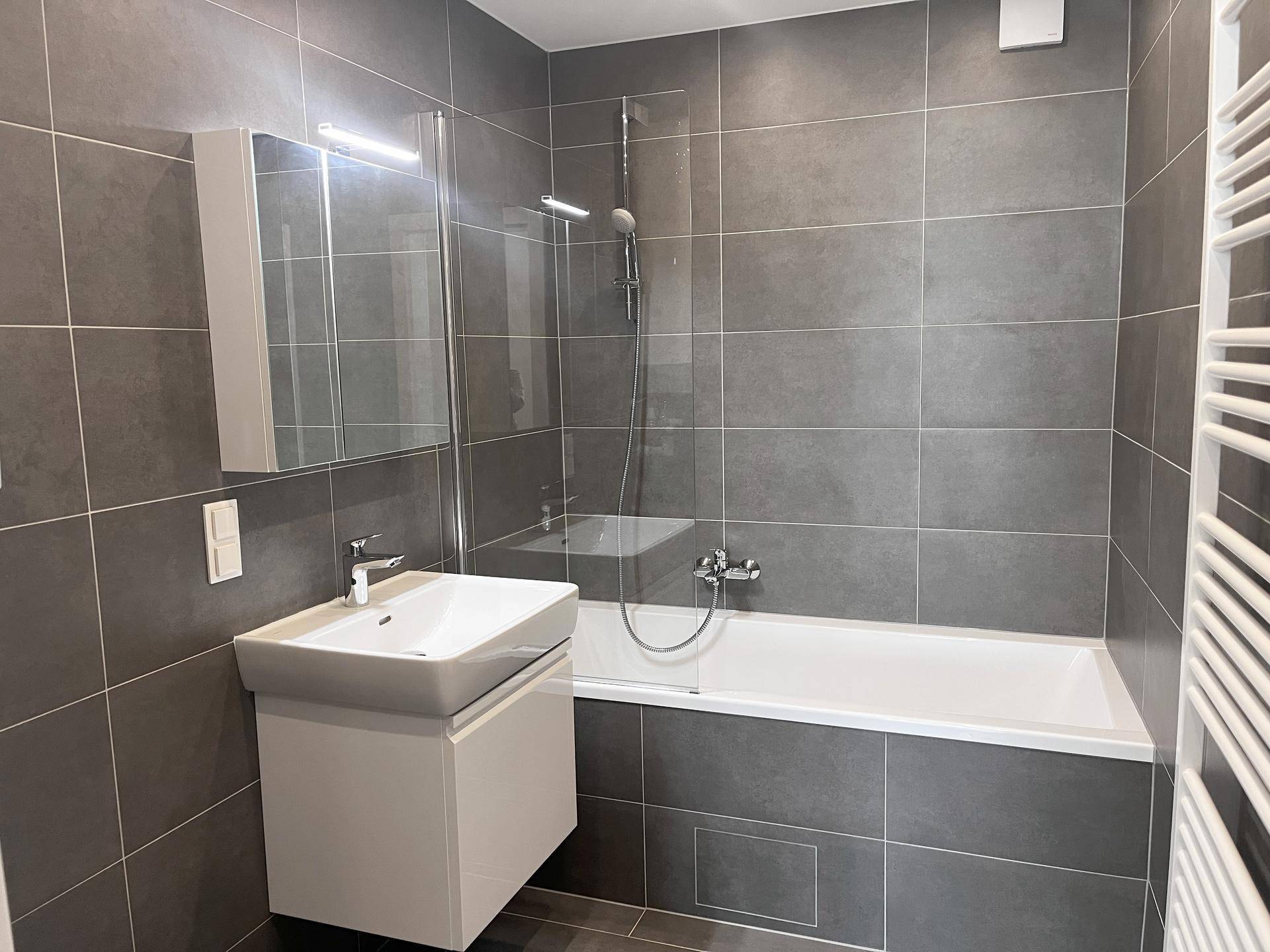 Modernes Badezimmer mit Badewanne, Waschtisch und grauen Fliesen.