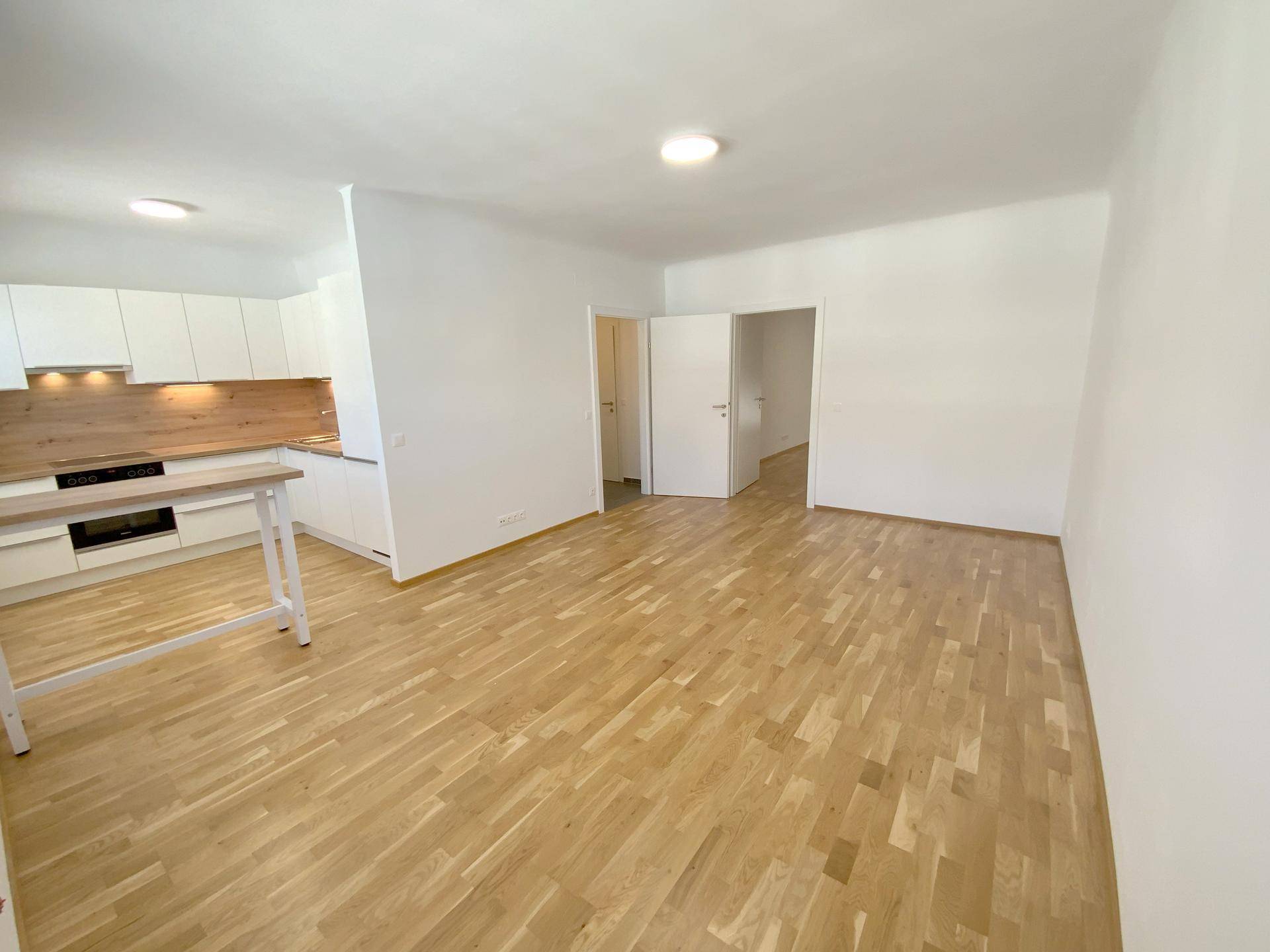 Leerer offener Wohnbereich mit neuer Einbauküche und hellem Parkettboden.