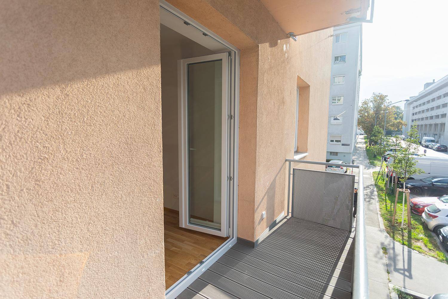 Kleiner Balkon mit modernem Bodenbelag und Blick auf die Straße und umliegende Gebäude.