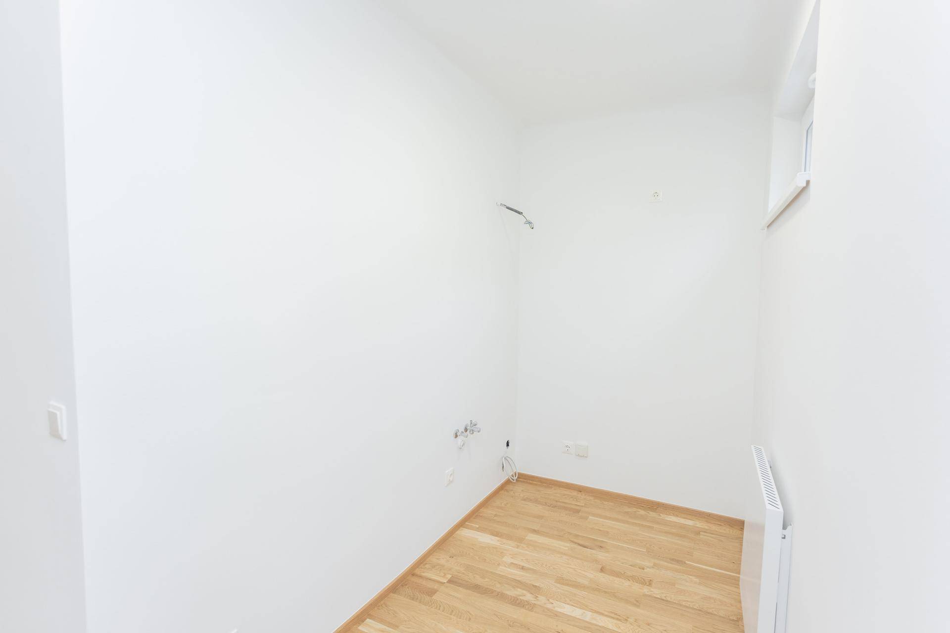 Kleiner, heller Raum mit Holzboden und weiß gestrichenen Wänden, ideal als Abstellraum.