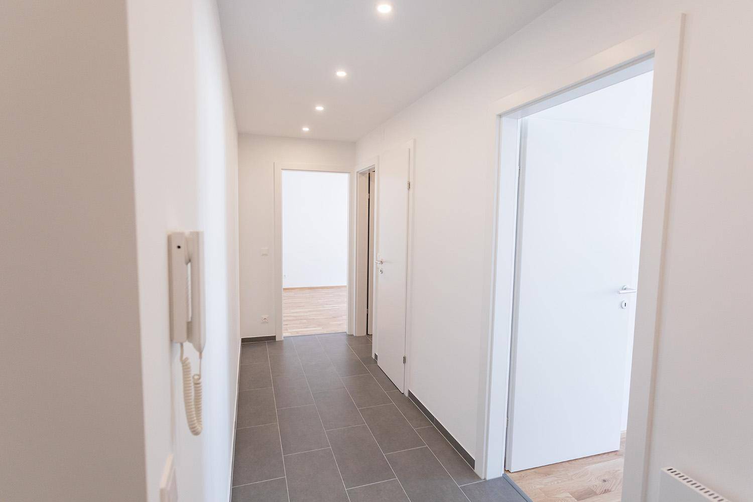 Heller Flur mit grauen Fliesen und Blick in angrenzende Zimmer, offen und einladend.