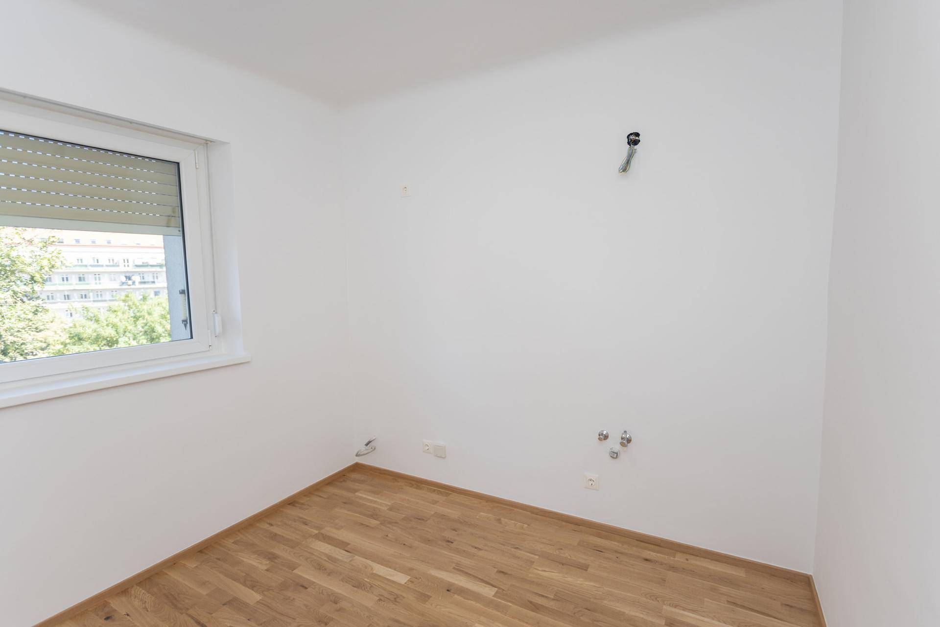 Leerer Raum mit Holzboden und Anschlüssen für eine zukünftige Küche oder Waschküche.