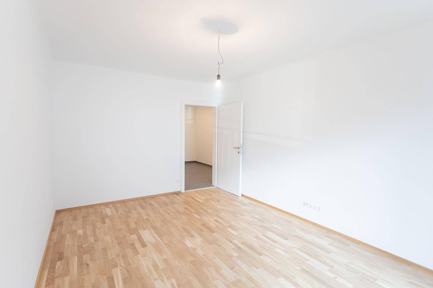 Helles Zimmer mit Parkettboden und weiß gestrichenen Wänden, bereit zur individuellen Gestaltung.