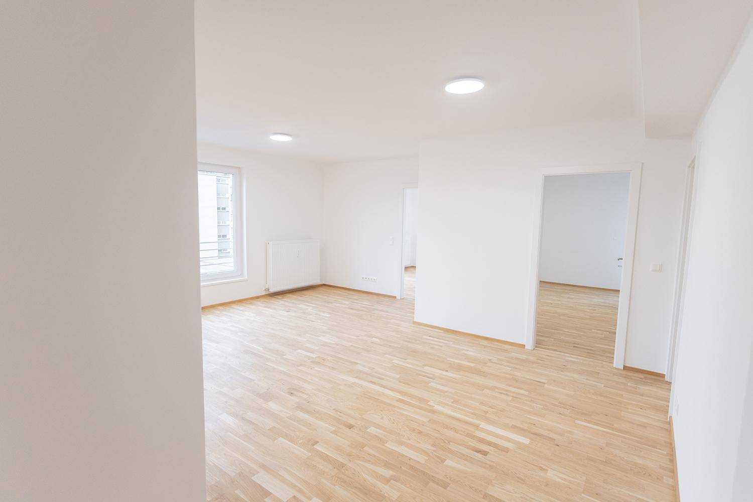 Geräumiger, heller Raum mit Holzboden und großen Fenstern, bereit zur Einrichtung.