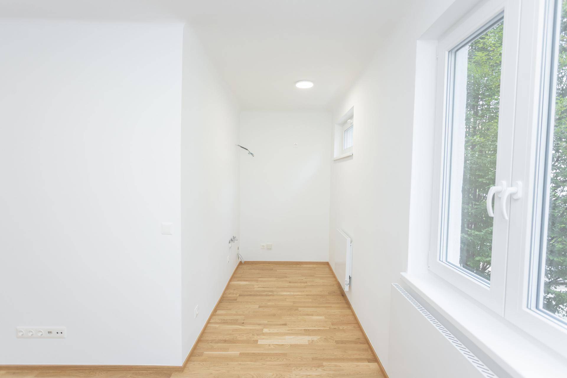 Langer, heller Raum mit Holzboden und Fenster, bietet vielseitige Nutzungsmöglichkeiten.