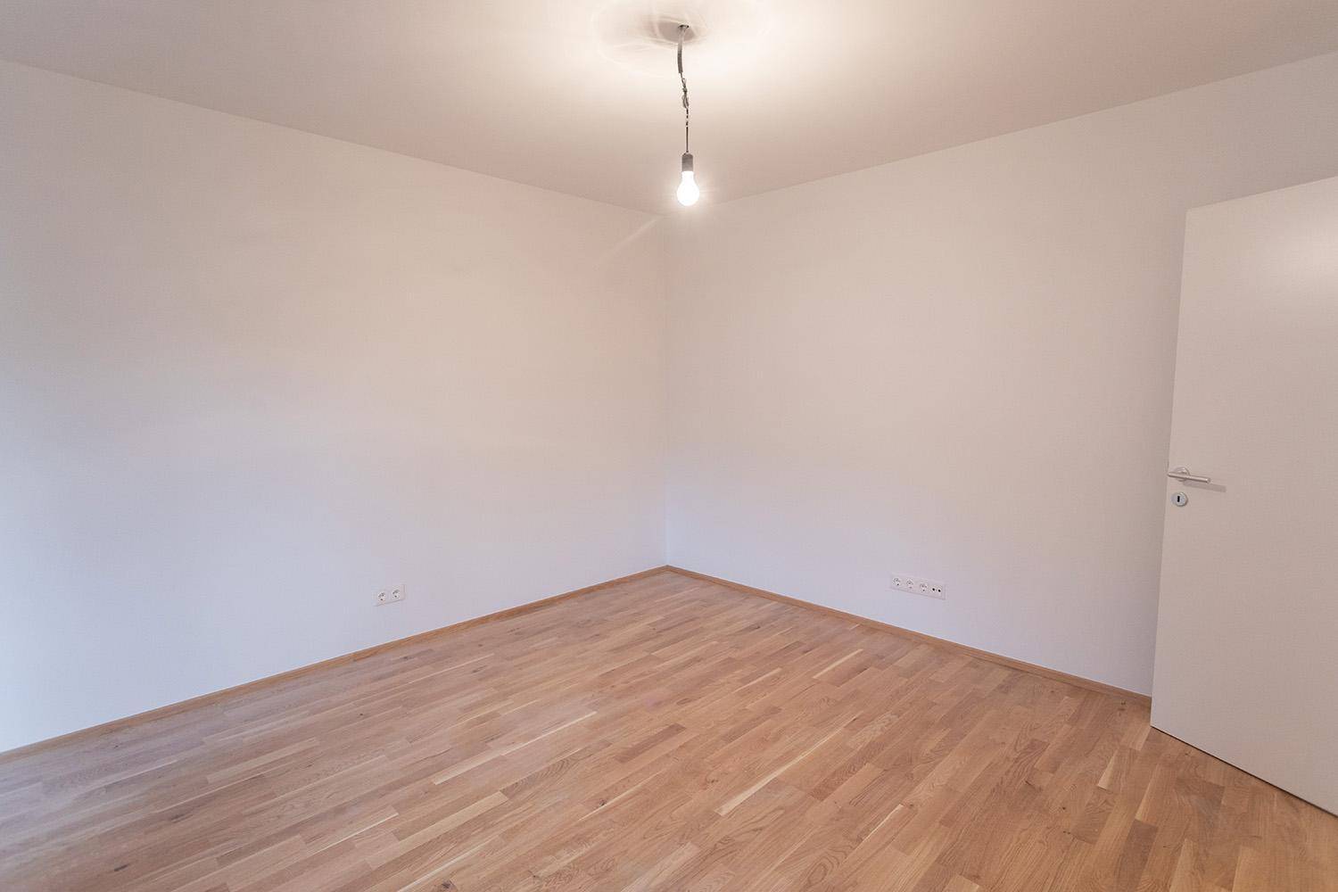 Leeres Schlafzimmer mit hellem Holzfußboden und weißen Wänden, bereit zur individuellen Gestaltung.