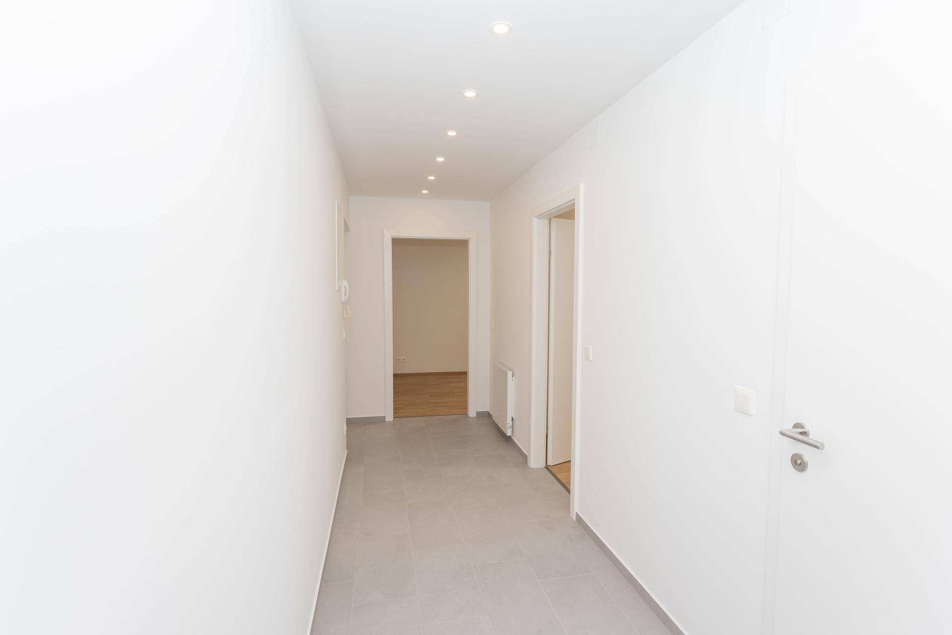 Langer, heller Flur mit grauen Fliesen, der zu den verschiedenen Zimmern der Wohnung führt.