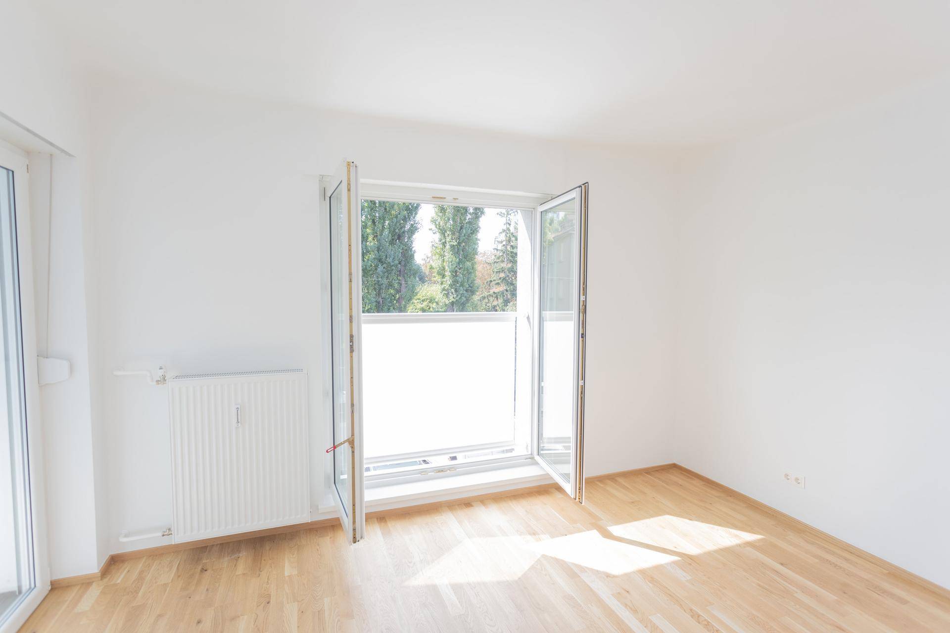 Geräumiges, helles Zimmer mit Parkettboden und geöffnetem Fenster mit Blick ins Grüne.