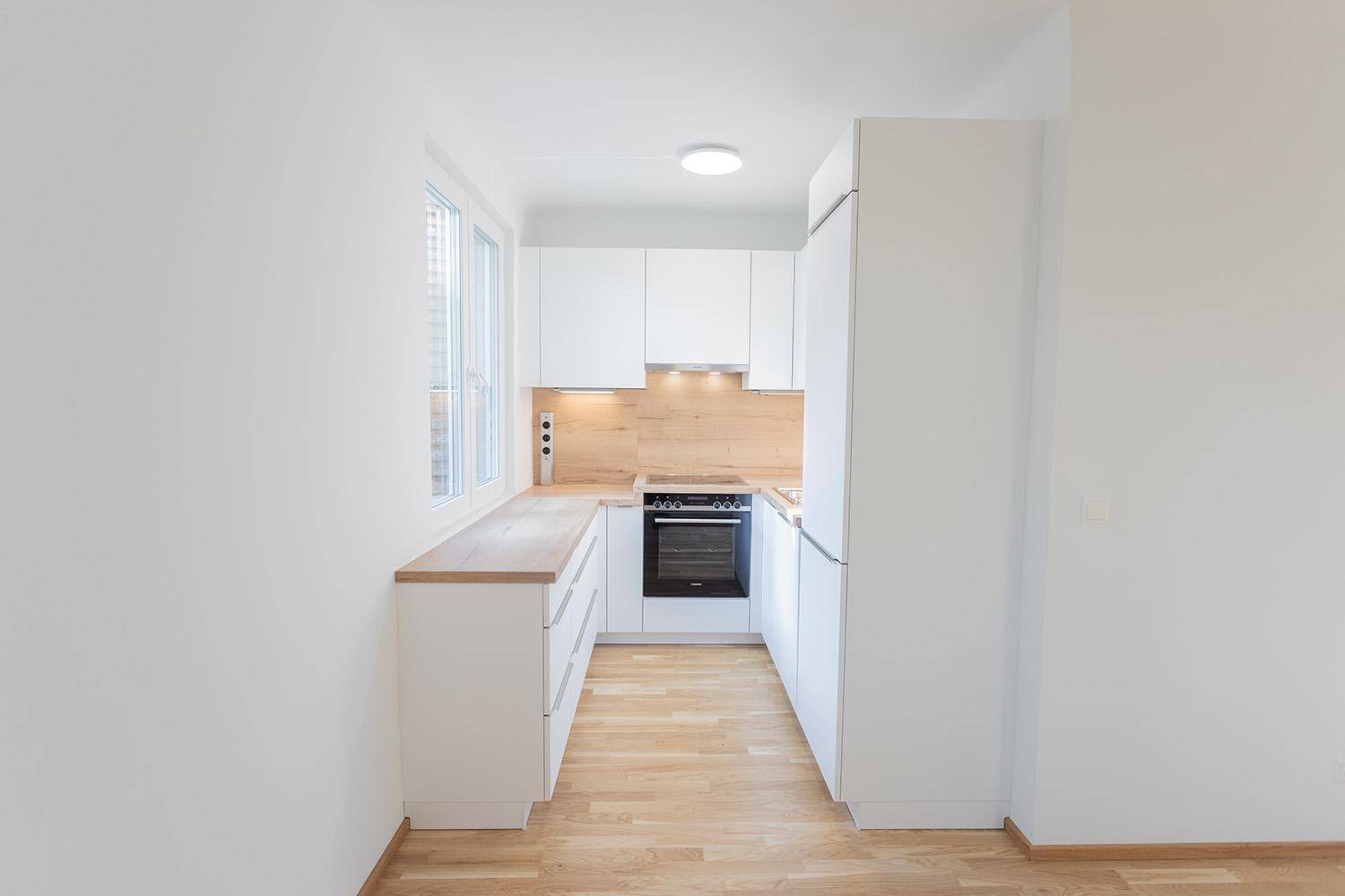 Moderne Einbauküche mit weißen Schränken, Holzarbeitsplatte und integrierten Geräten, inklusive Fenster.
