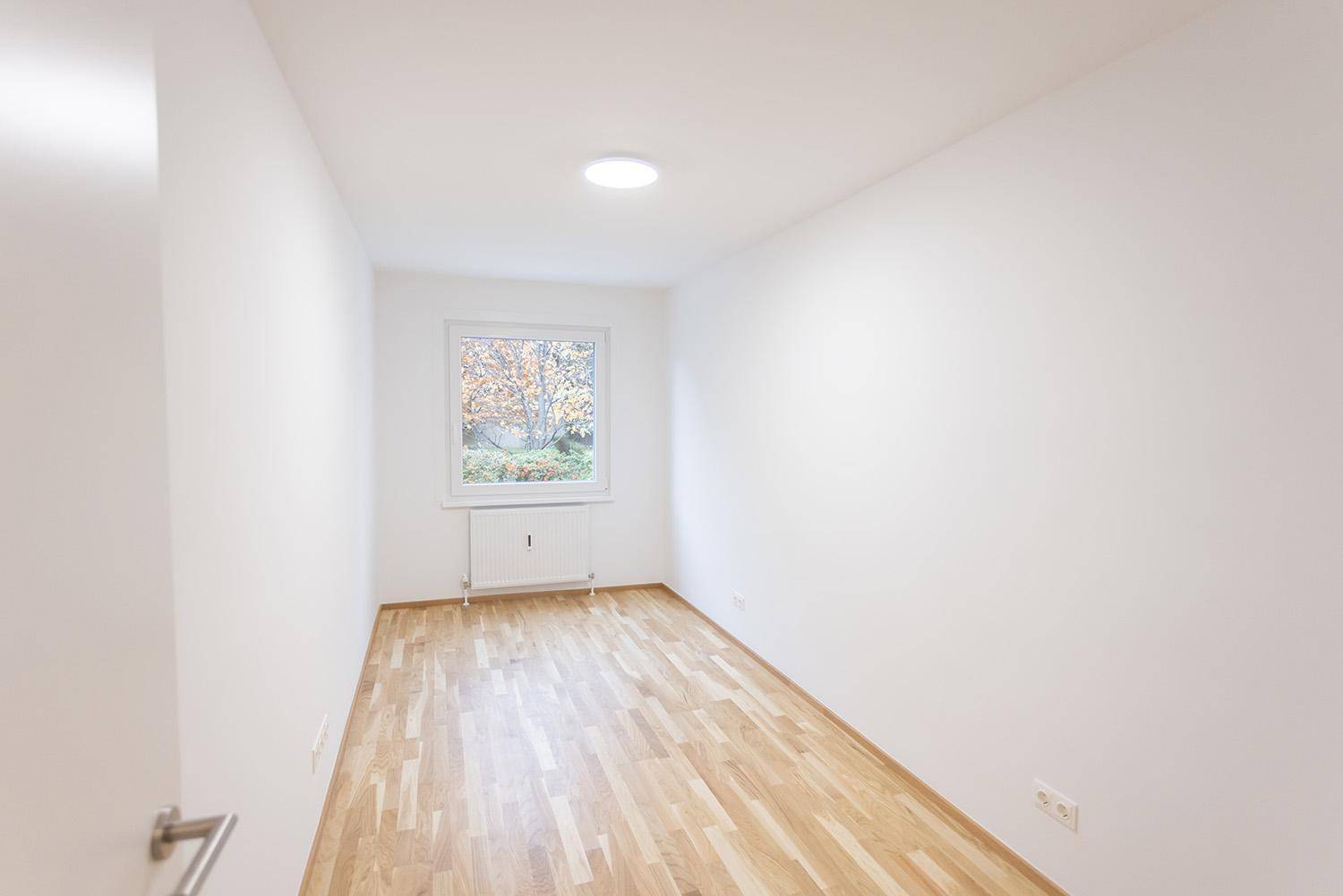 Helles, unmöbliertes Zimmer mit Parkettboden und Blick ins Grüne, ideal als Schlafzimmer.