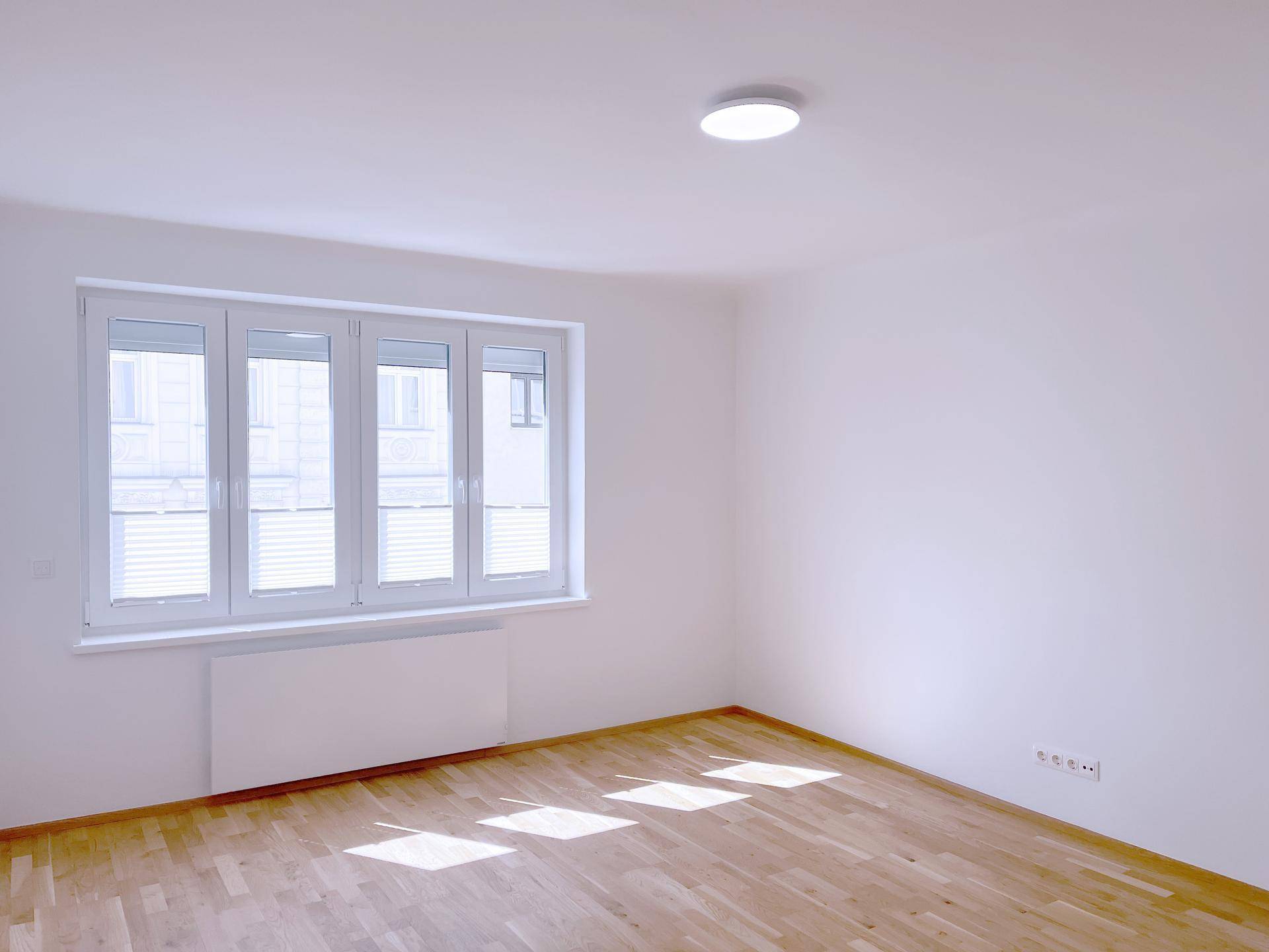 Heller Raum mit Parkettboden und Fenster mit Jalousien.