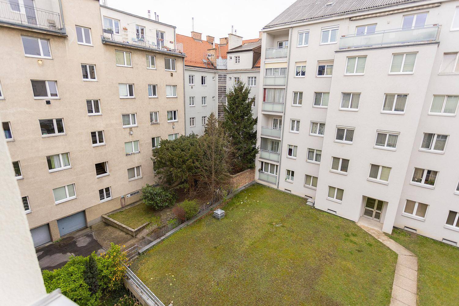 Blick auf den grünen Innenhof mit Rasenfläche und Bäumen, umgeben von Wohngebäuden.
