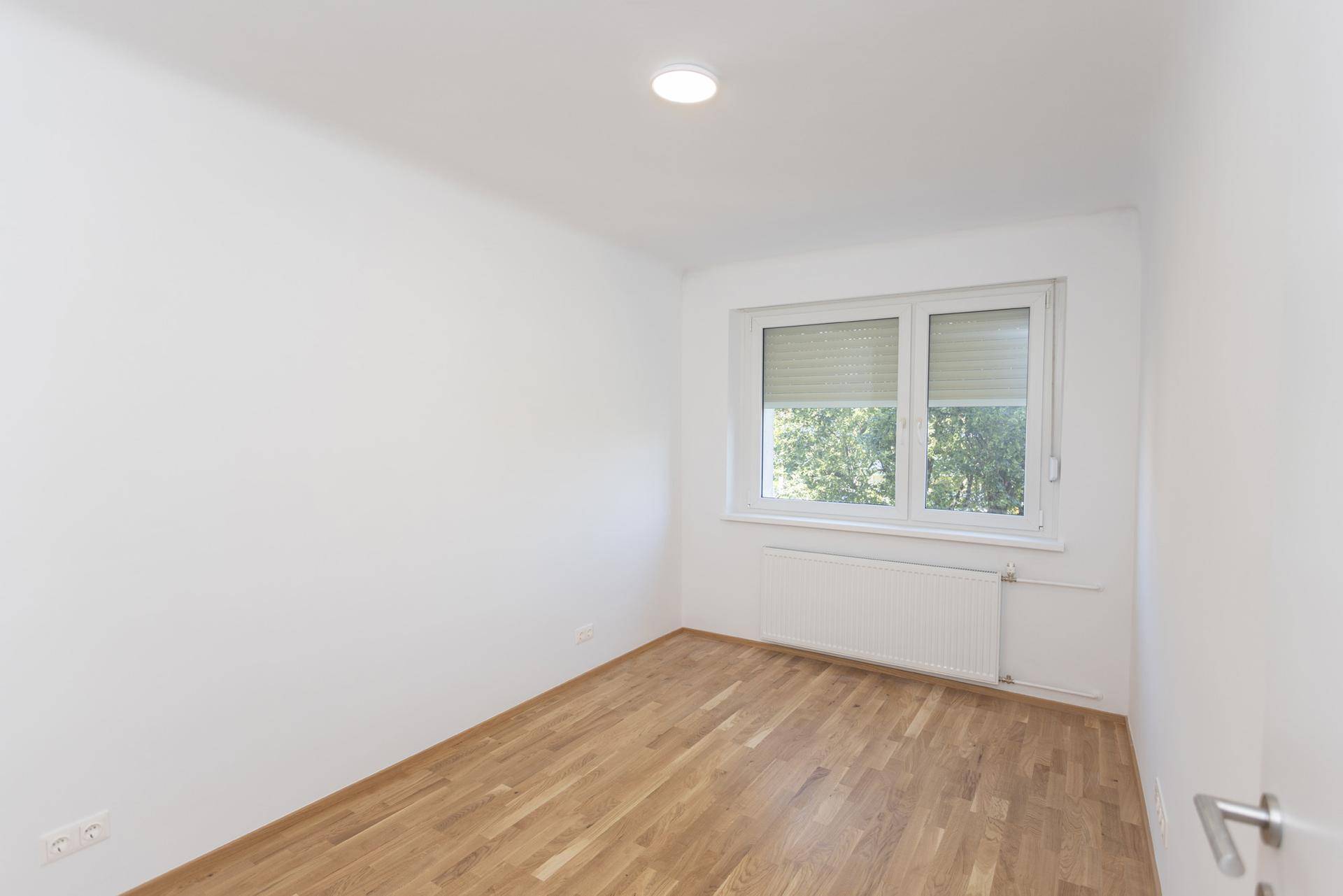Leeres Schlafzimmer mit Holzboden und großem Fenster, ideal für individuelle Einrichtung.
