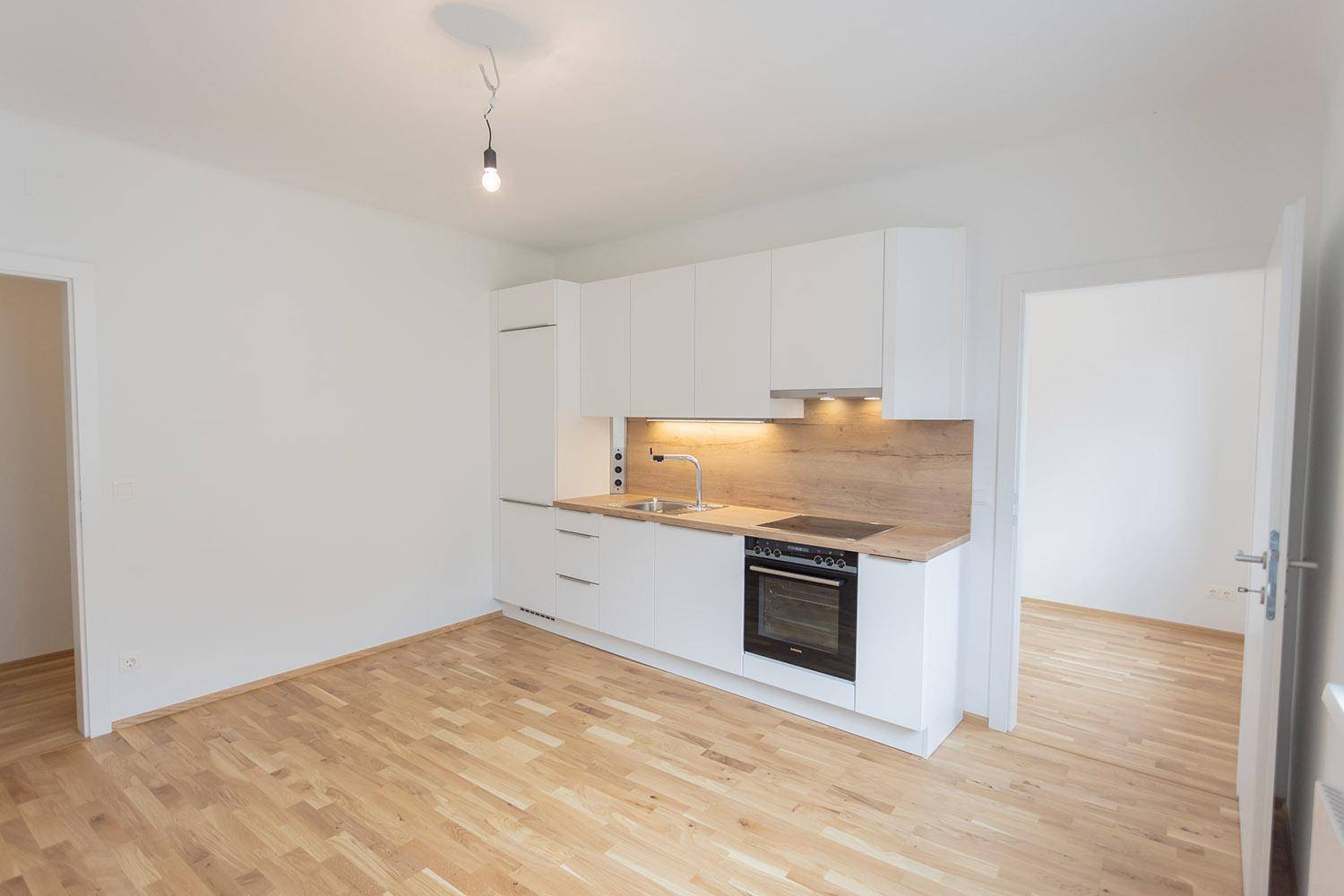 Offener Wohnbereich mit neuer Einbauküche und Holzboden, der den Blick in einen weiteren Raum freigibt.