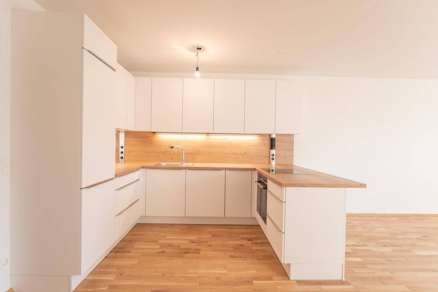 Moderne Einbauküche mit weißen Schränken, Holz-Arbeitsplatten und integrierten Geräten.