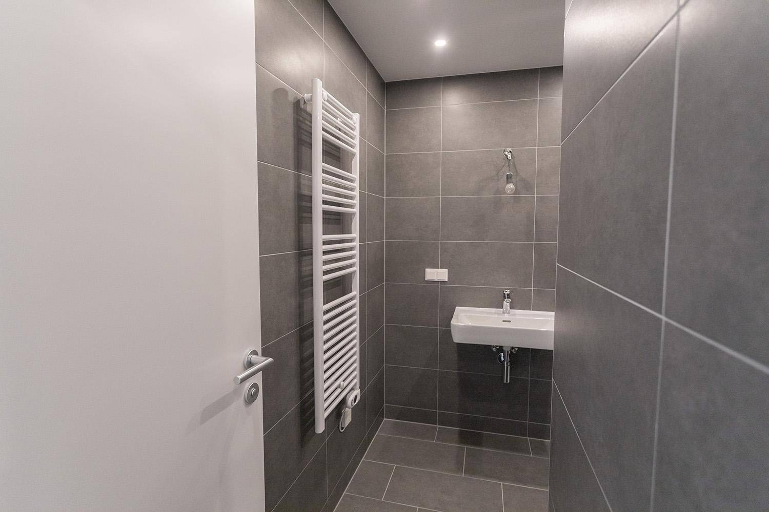 Modernes Badezimmer mit Handtuchheizkörper, Waschbecken und grauen Fliesen, schlicht und funktional.