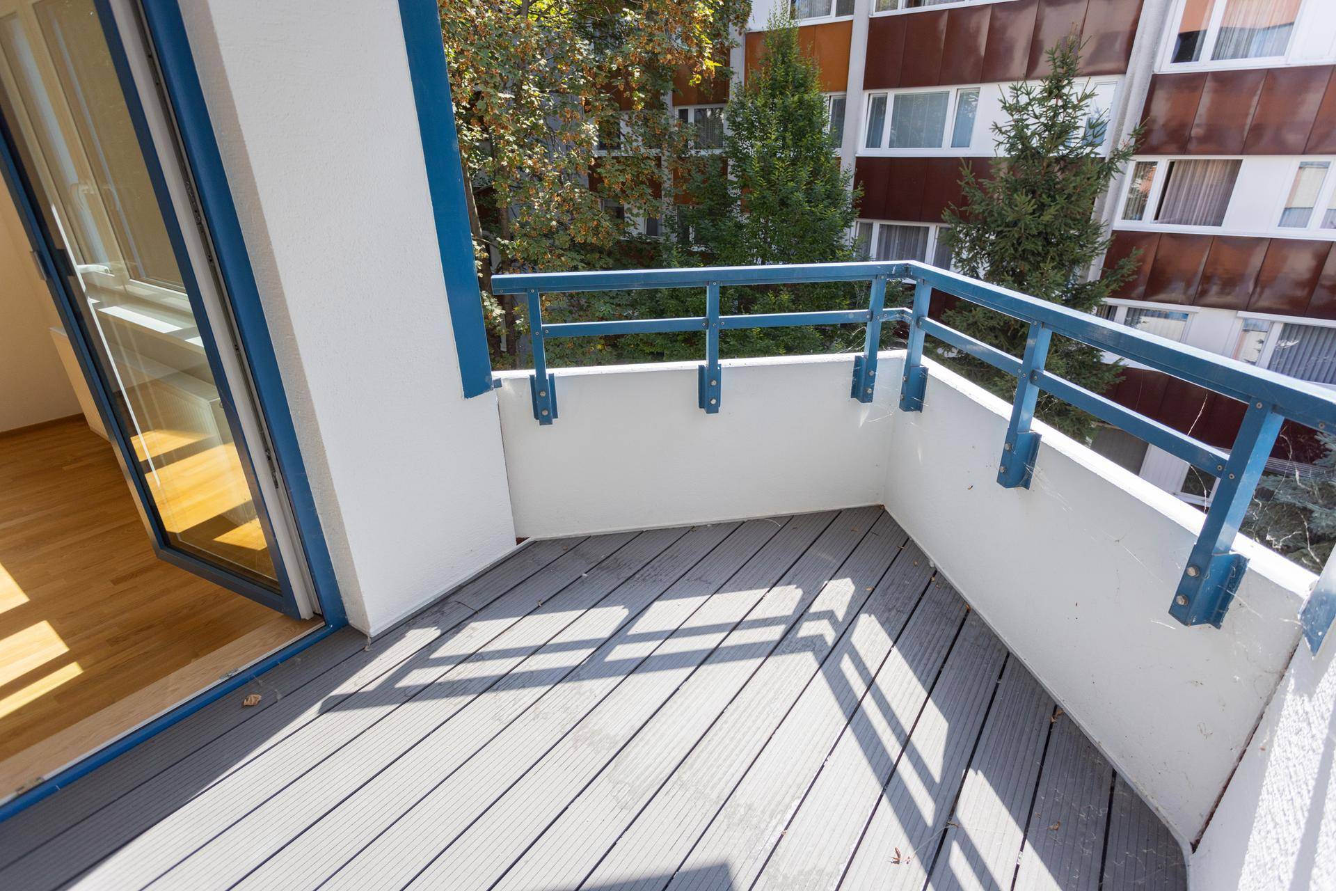 Geräumiger Balkon mit modernem Dielenboden und blauer Brüstung, zugänglich durch eine Glastür.