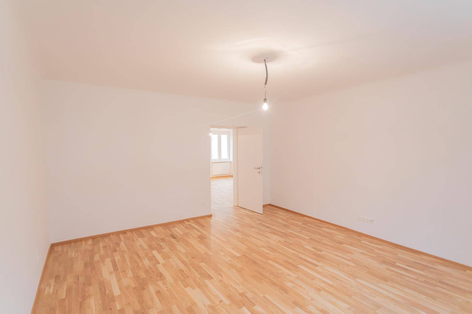 Geräumiges Zimmer mit Parkettboden und offener Verbindung zu einem angrenzenden Raum.