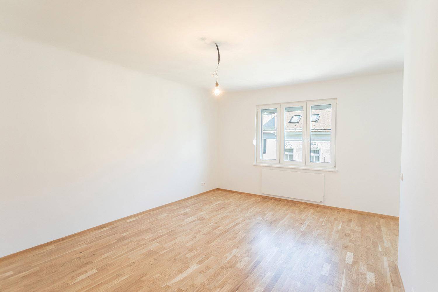Heller, leerer Raum mit Parkettboden und großen Fenstern, ideal als Wohnzimmer.