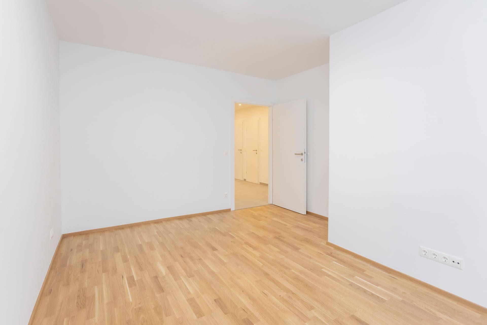 Helles Schlafzimmer mit Parkettboden und Zugang zu einem angrenzenden Raum.