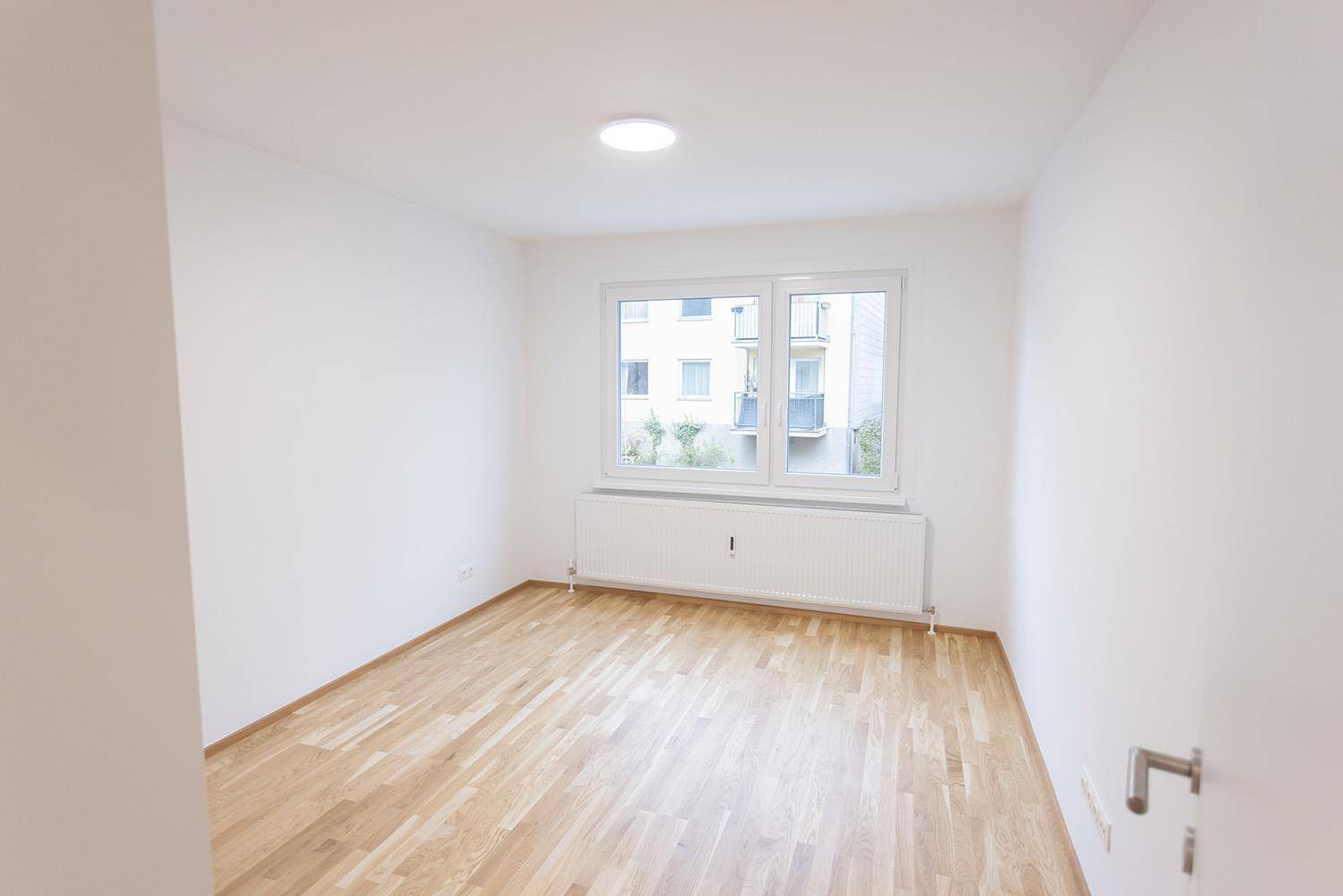 Geräumiges, unmöbliertes Zimmer mit Parkettboden und zwei Fenstern, bietet viel Tageslicht.