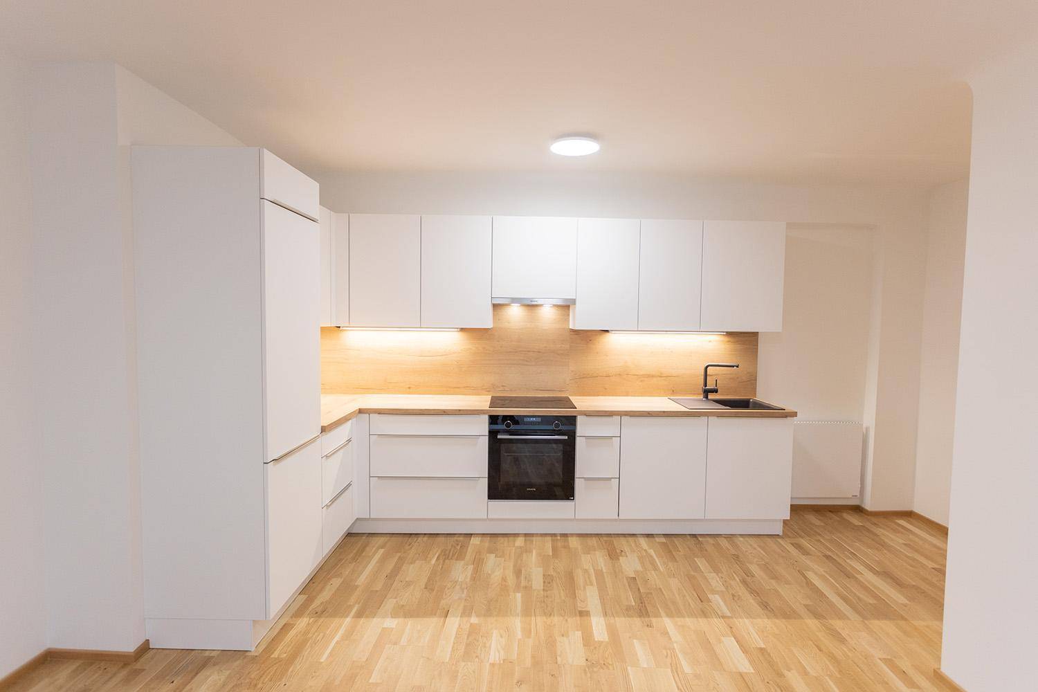 Neue, helle Küche mit weißen Fronten, Holzdetails und modernen Einbaugeräten.
