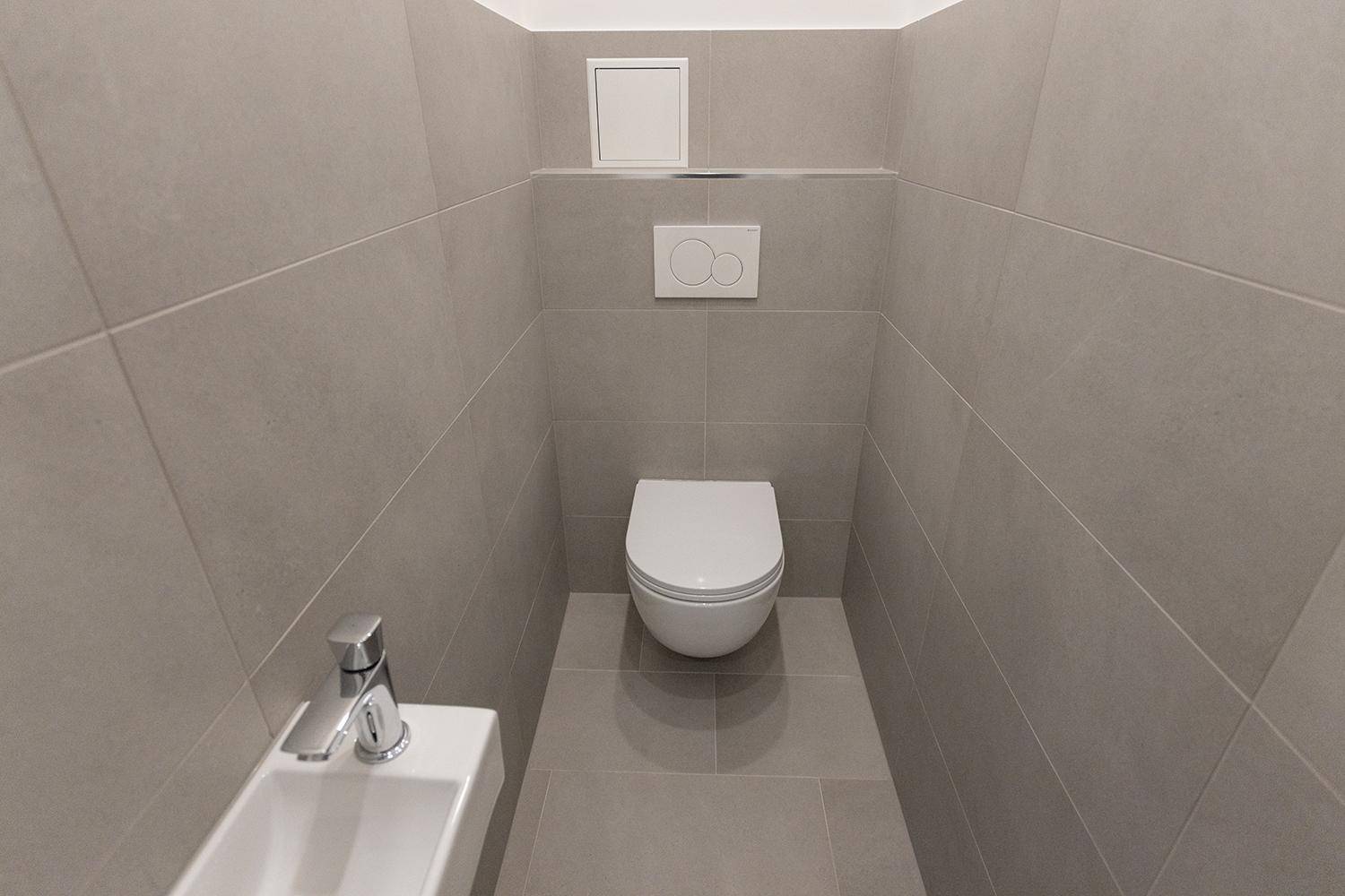 Modernes Gäste-WC mit wandhängender Toilette und kleinem Waschbecken in Grau.