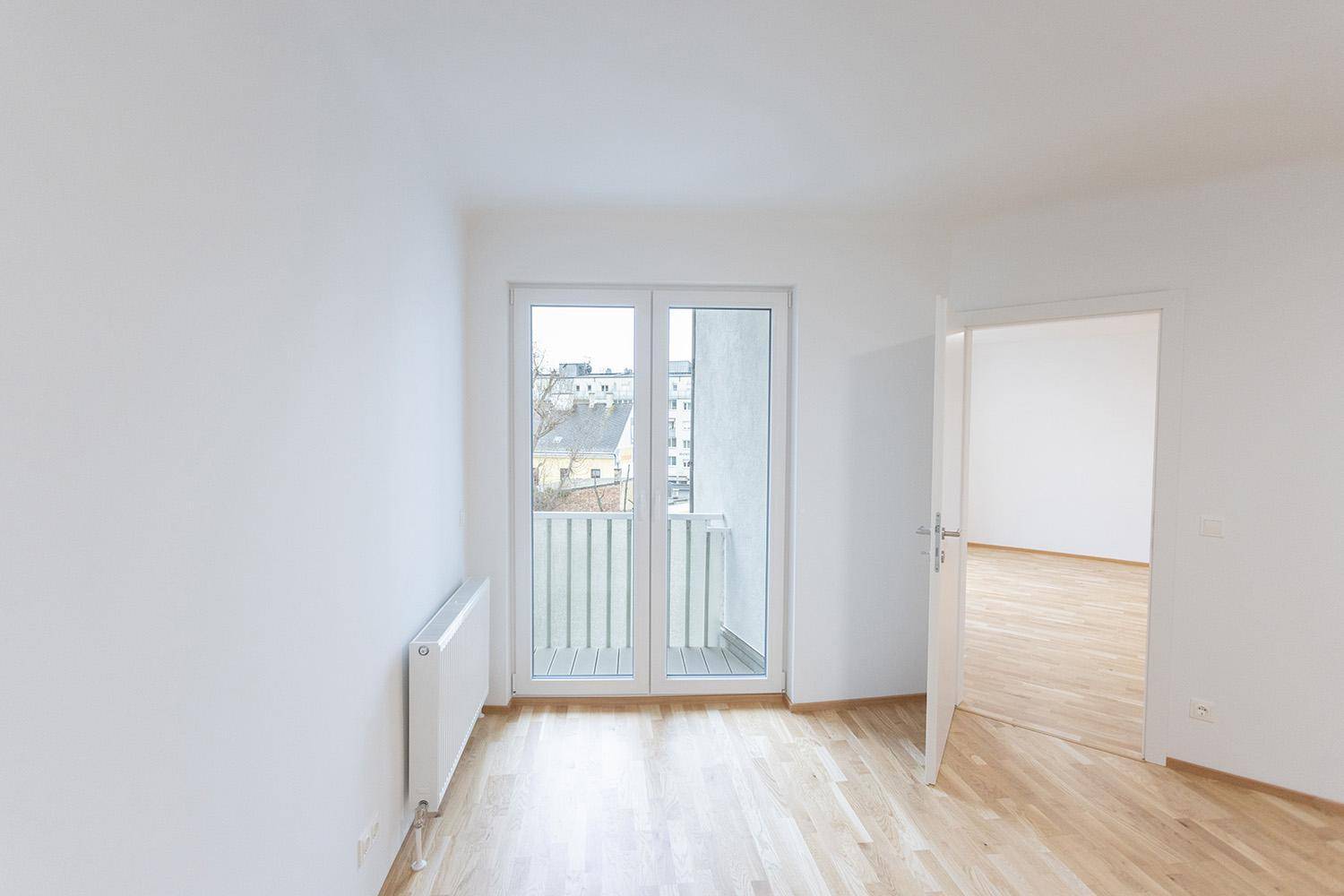 Helles Schlafzimmer mit Holzboden und Zugang zu einem französischen Balkon, bereit zur Einrichtung.