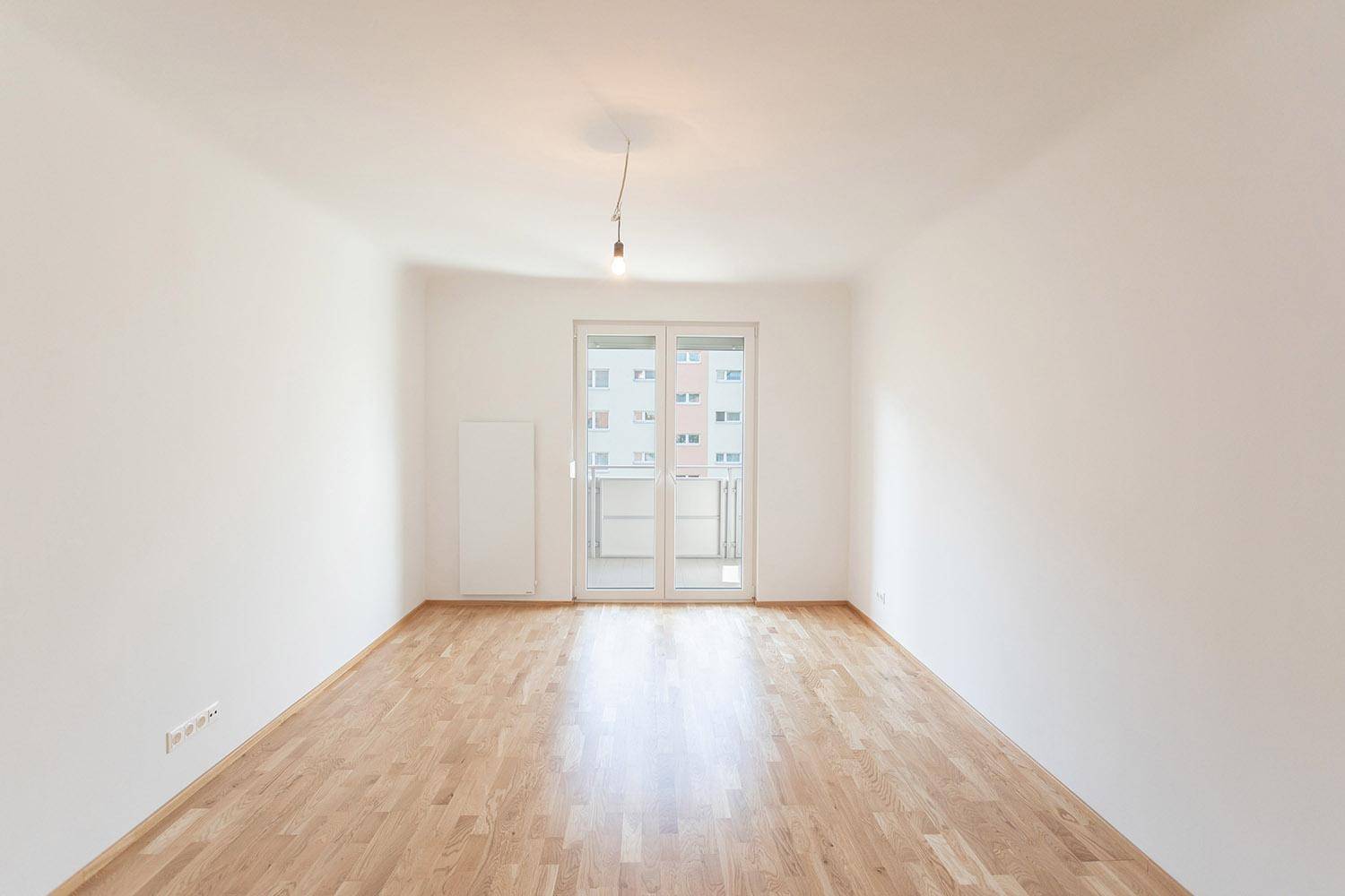 Geräumiger, heller Raum mit Parkettboden und Zugang zu einem Balkon.