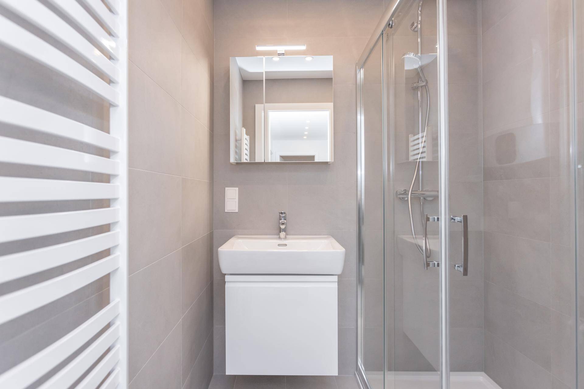 Modernes Badezimmer mit Duschkabine, Waschtisch und beheiztem Handtuchhalter.