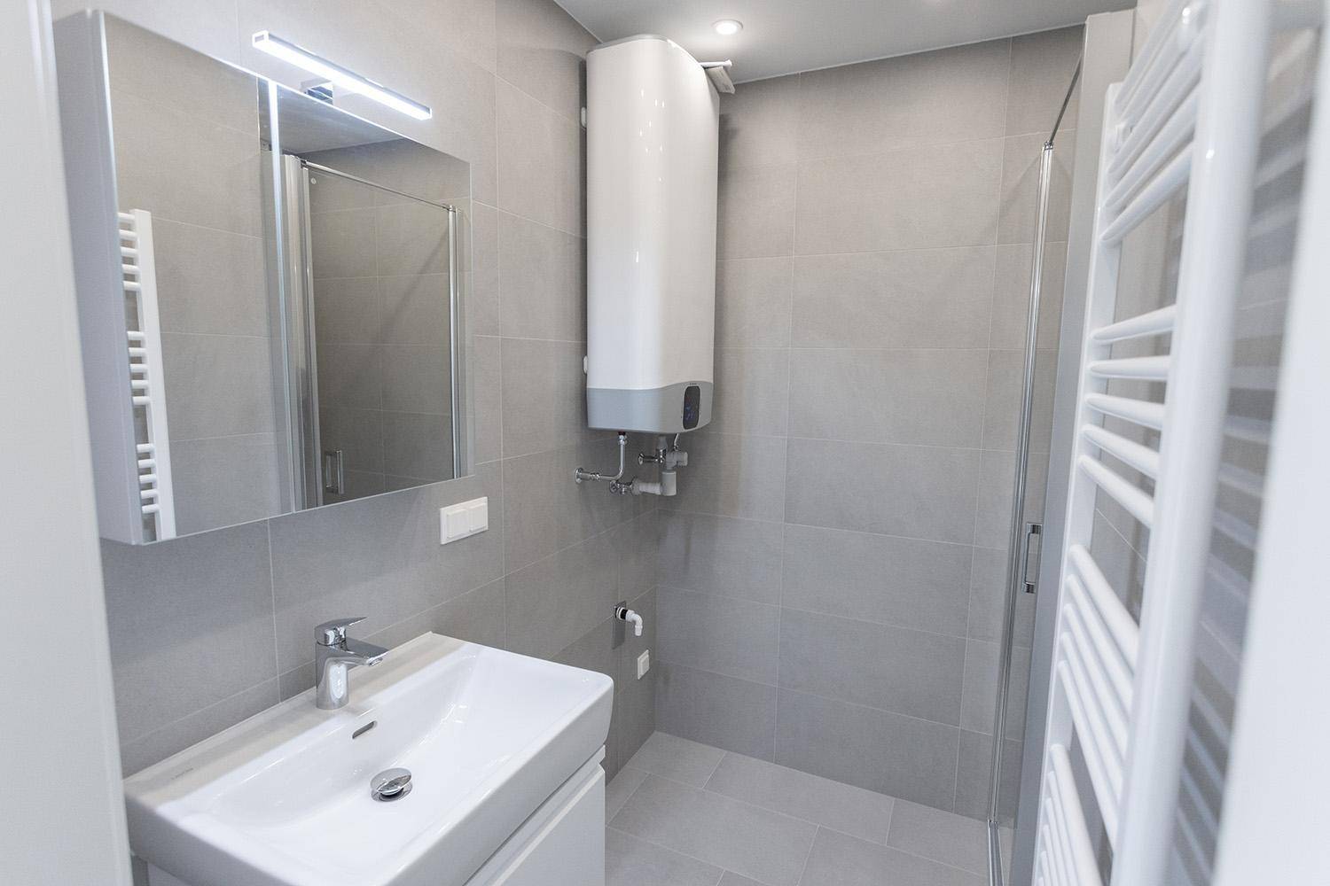 Modernes Badezimmer mit grauen Fliesen, Einzelwaschbecken, Duschkabine und Handtuchheizkörper.