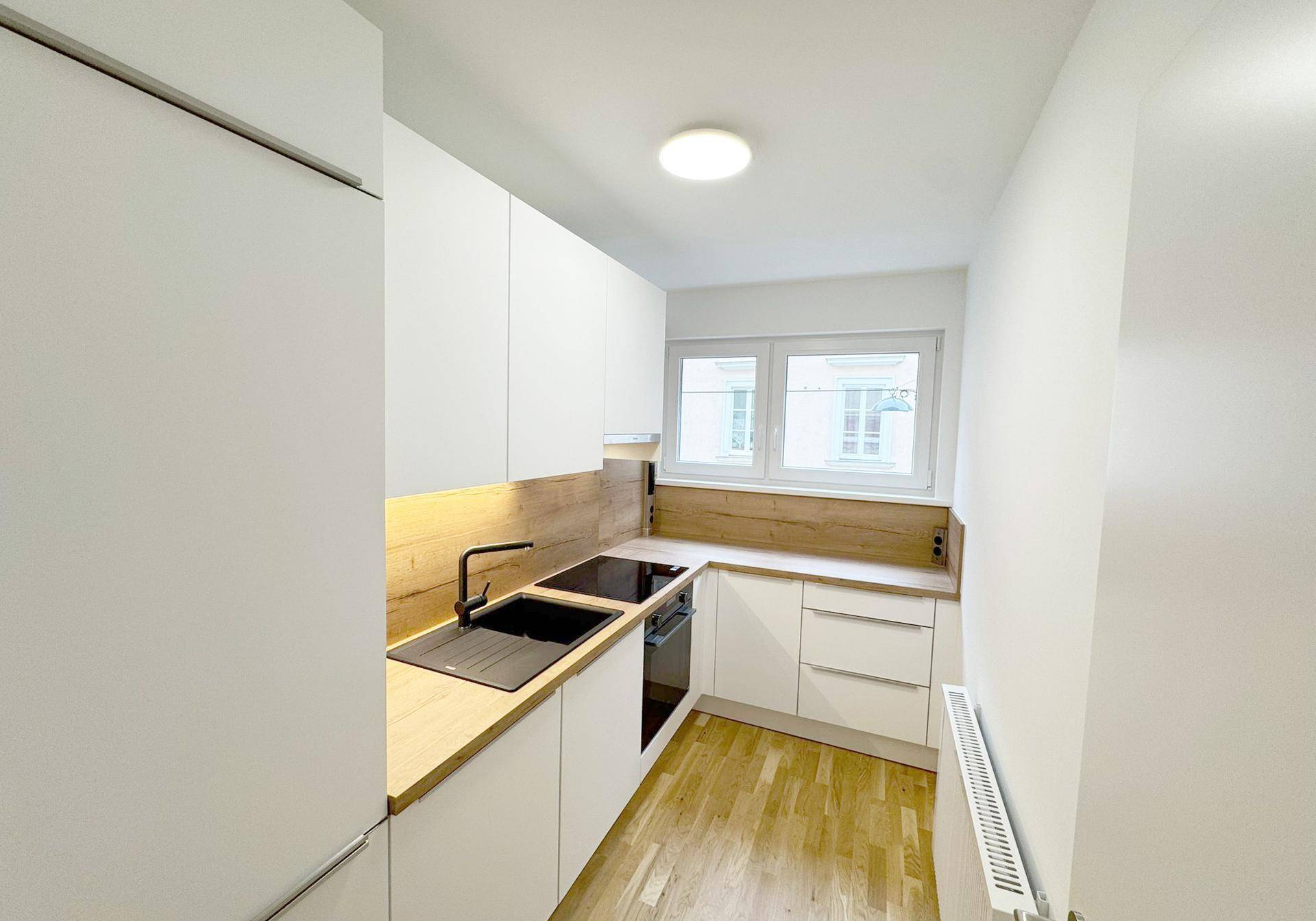 Moderne Küche mit weißen Schränken, Holz-Arbeitsplatte und Fenster, hell und funktional.
