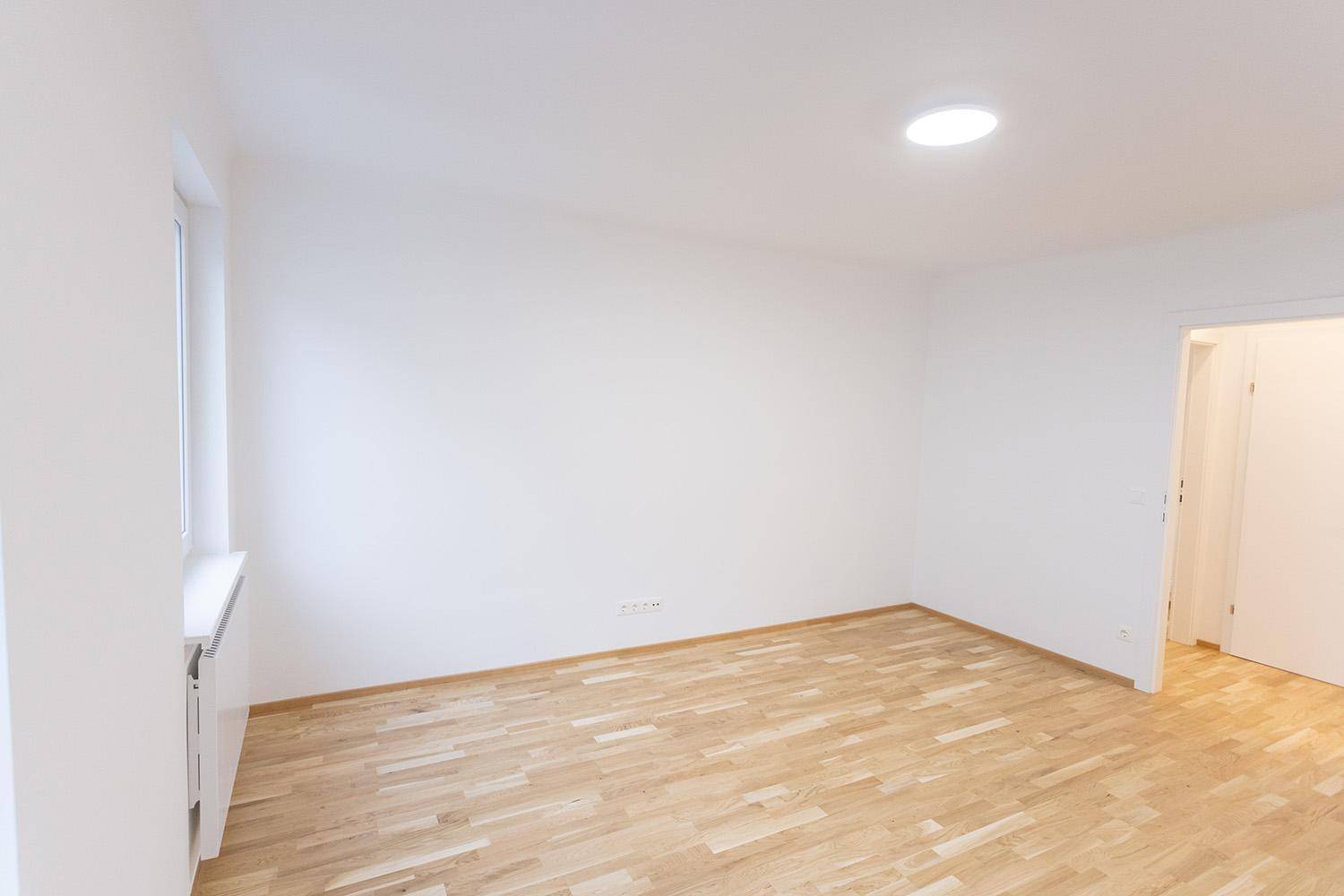 Helles, leeres Zimmer mit Holzboden und einem Fenster, vielseitig nutzbar.