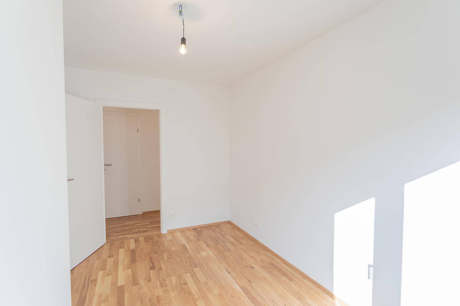 Leerer Raum mit hellem Parkettboden und weiß gestrichenen Wänden, bereit zur Nutzung.