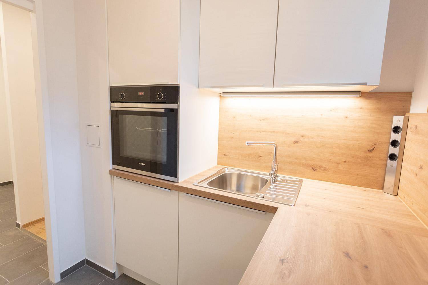 Moderne Küche mit weißen Unterschränken, Holzarbeitsplatte, Spüle und integriertem Backofen.