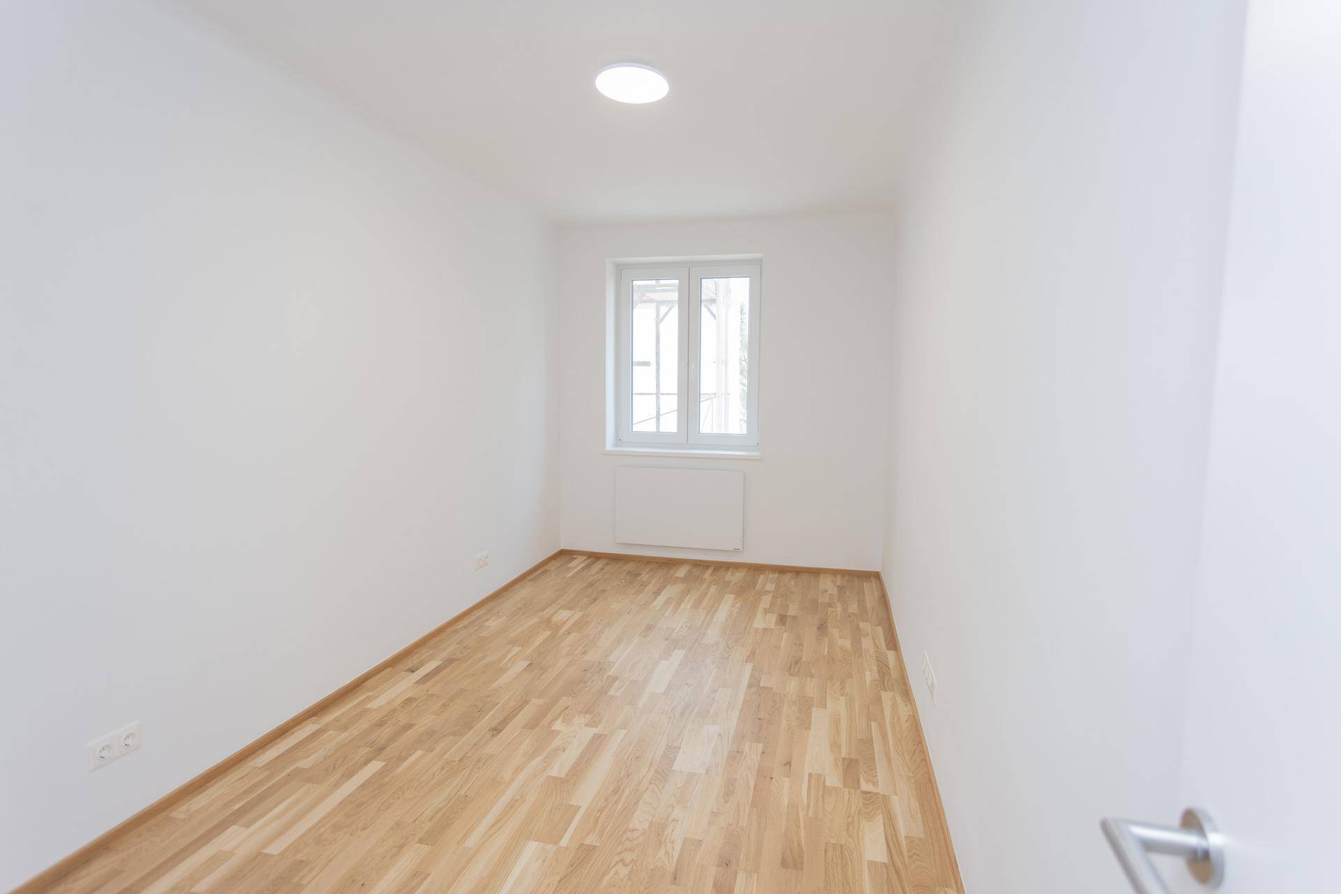 Helles Zimmer mit neuem Parkettboden und einem Fenster, bereit zum Einrichten.