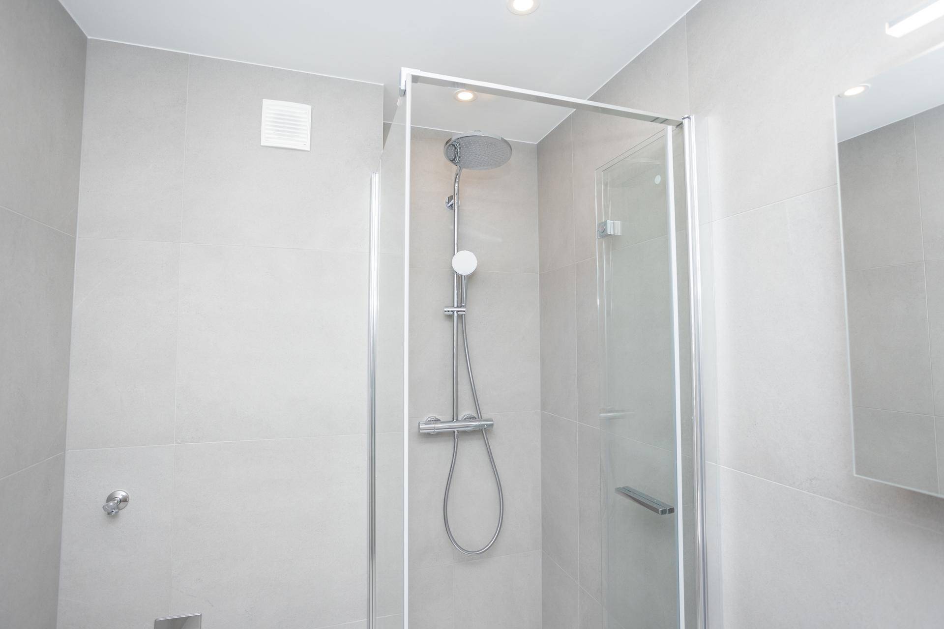 Detaillierte Ansicht der modernen Duschkabine mit Regendusche und grauen Fliesen im Badezimmer.
