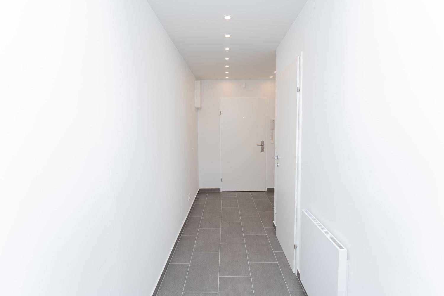 Langer, heller Flur mit grauen Fliesen und weiß gestrichenen Wänden, modern und schlicht.