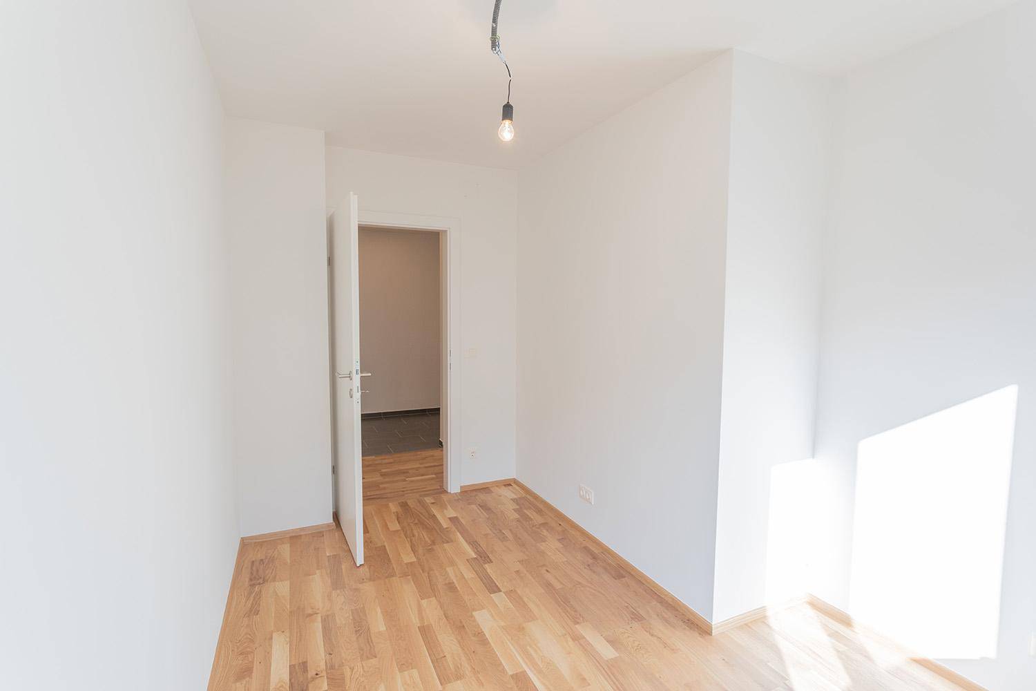 Leerer Raum mit hellem Parkettboden und weiß gestrichenen Wänden, ideal für verschiedene Nutzungen.