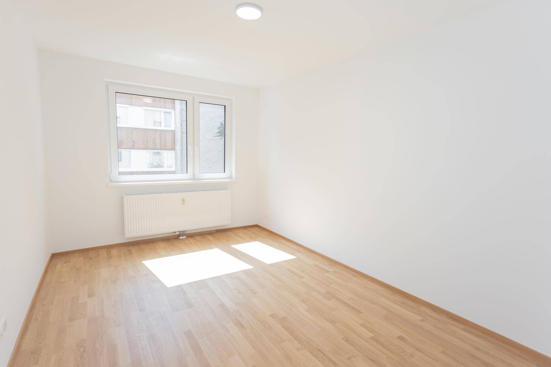 Leeres Zimmer mit hellem Parkettboden und weiß gestrichenen Wänden, vielseitig nutzbar.