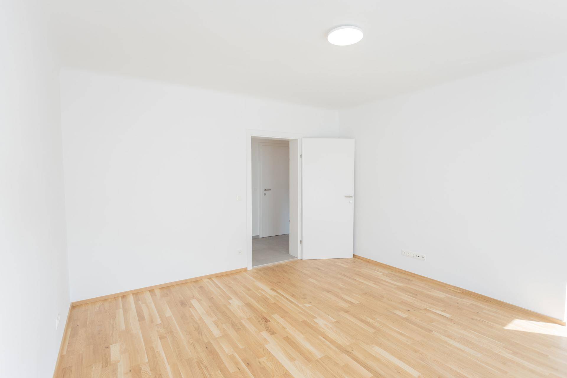 Leeres Zimmer mit hellem Parkettboden und weiß gestrichenen Wänden, bereit zur Einrichtung.