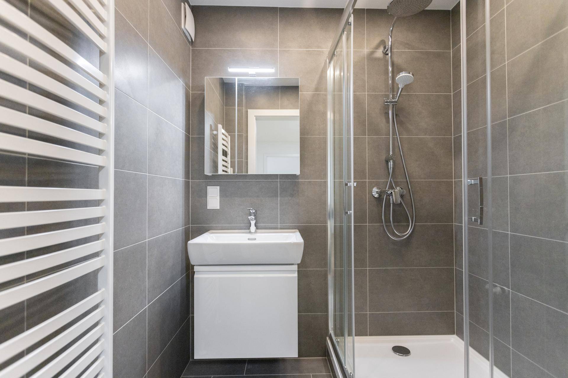 Modernes Badezimmer mit Duschkabine, Waschbecken und beheiztem Handtuchhalter in Grau.