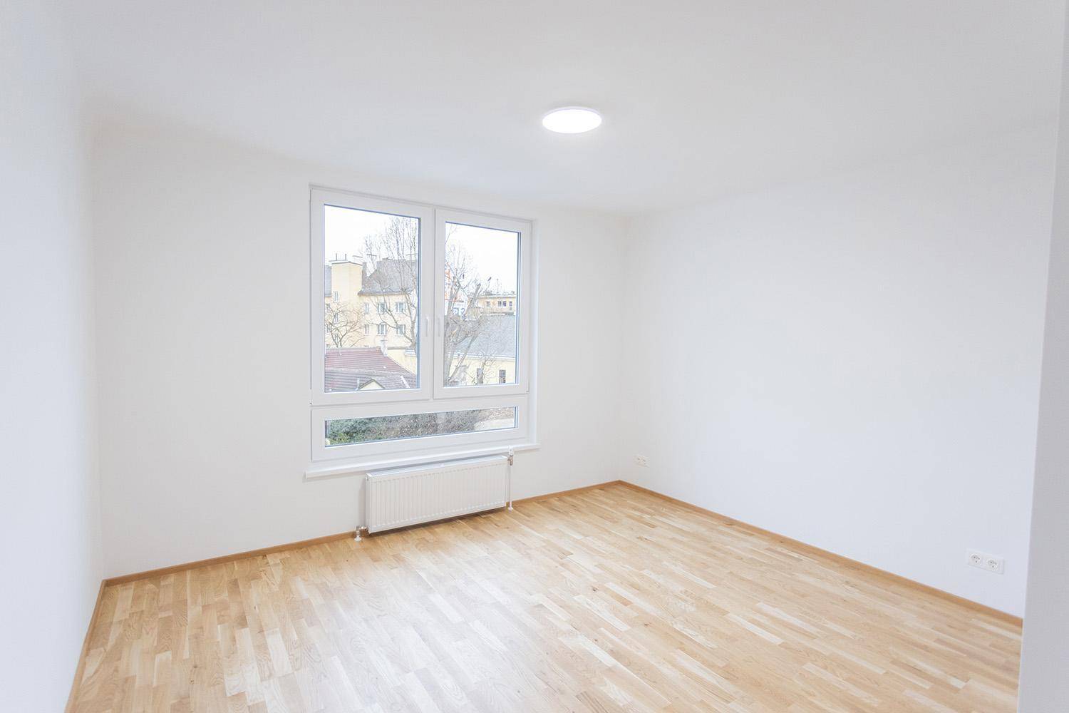Helles Wohnzimmer mit Holzboden und großem Fenster, das viel Tageslicht hereinlässt.
