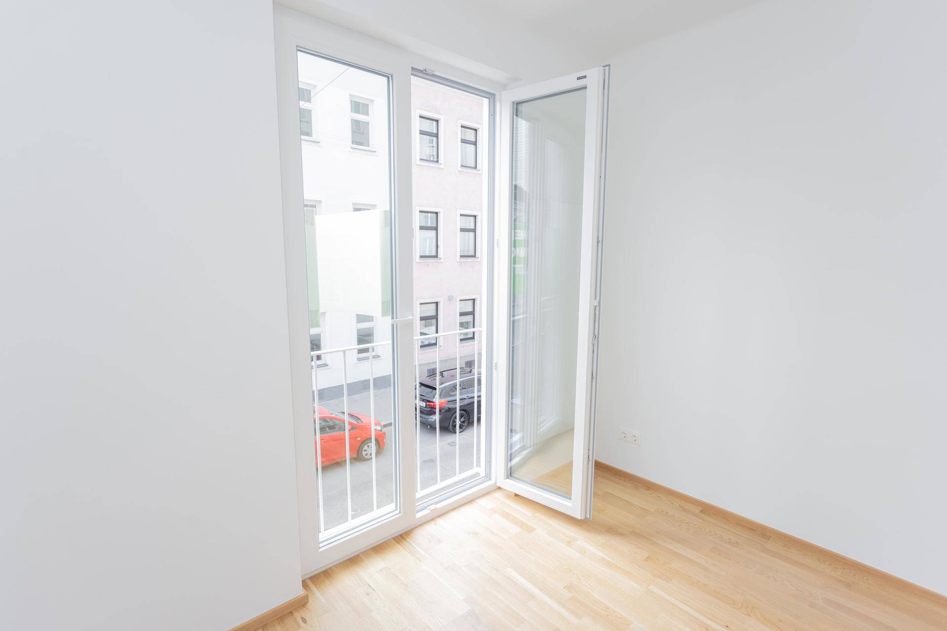 Heller, leerer Raum mit Holzfußboden und französischem Balkon mit Blick auf die Straße.